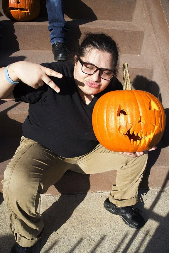 Young woman sitting on stairs holding a carved Halloween pumpkin and making a peace sign.
