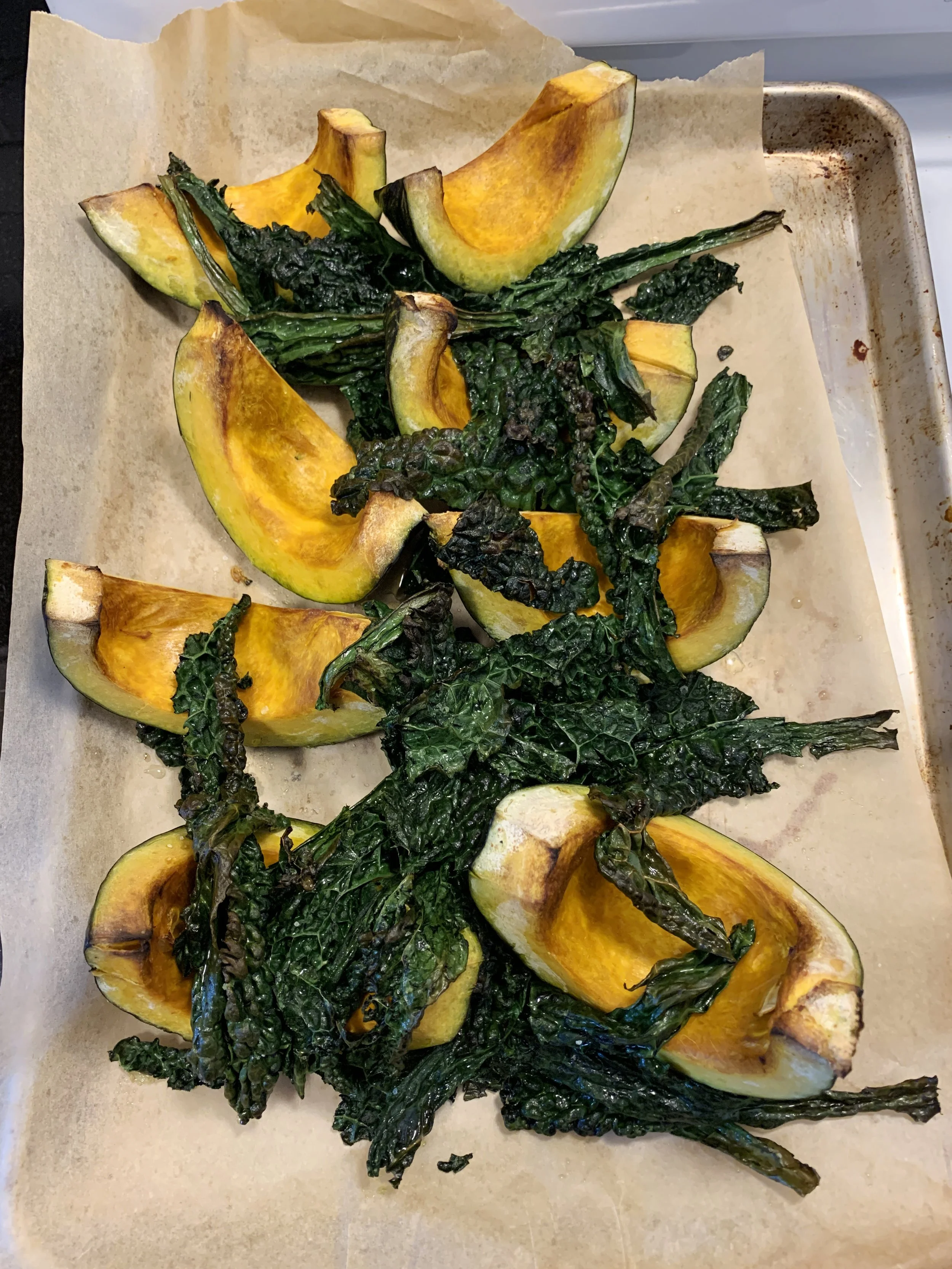 Roasted acorn squash halves filled with caramelized kale on a baking sheet lined with parchment paper.