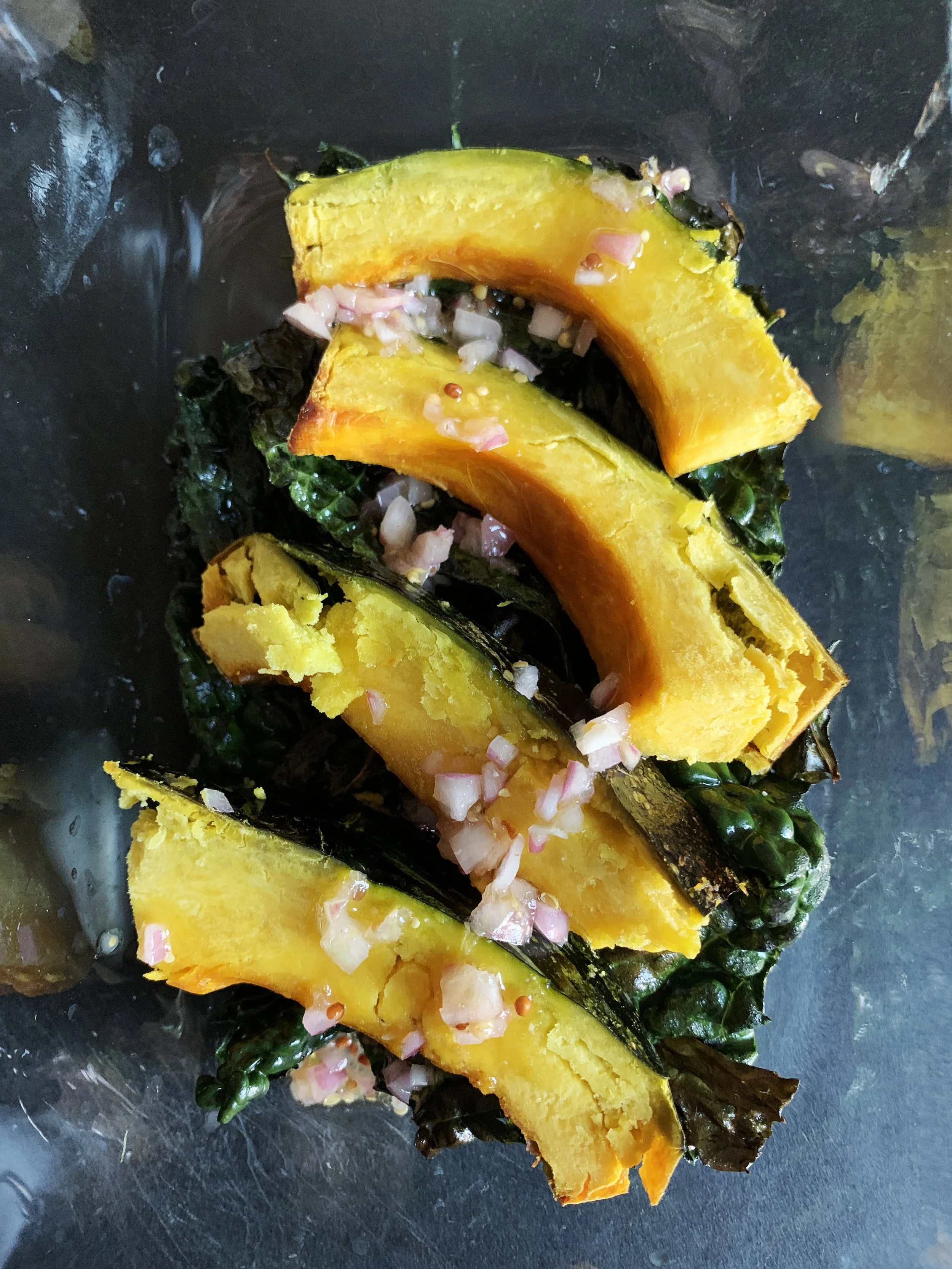 Roasted pumpkin slices topped with chopped red onions, placed on dark leafy greens.