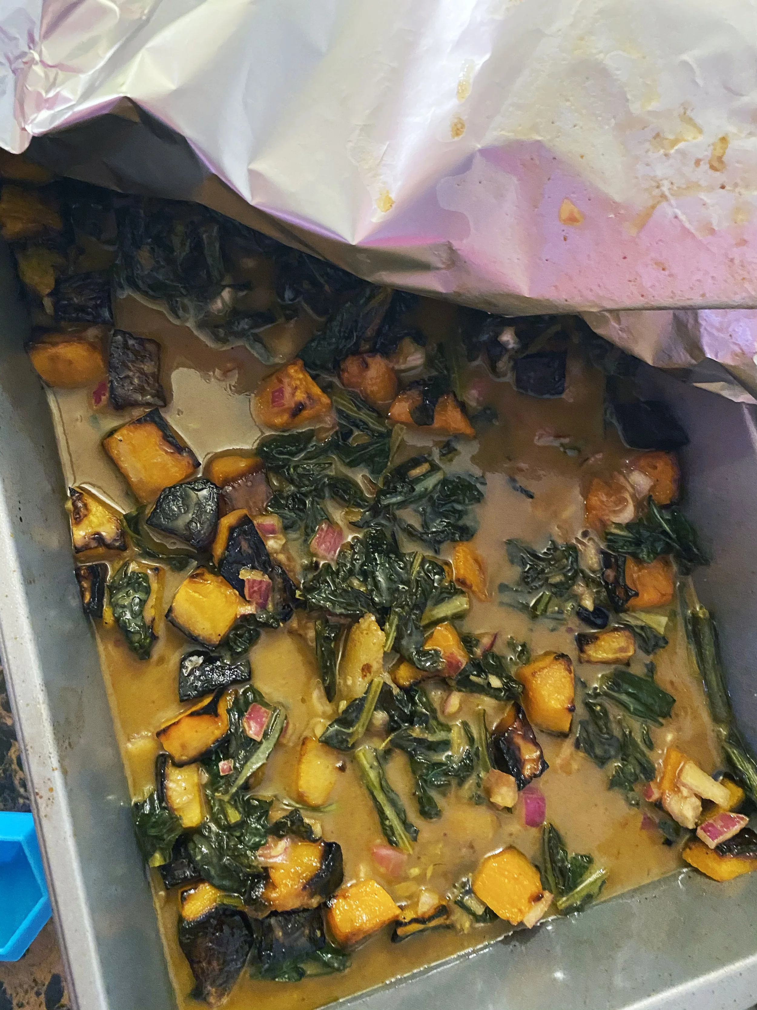 Roasted sweet potatoes and greens in a seasoned sauce in a baking tray