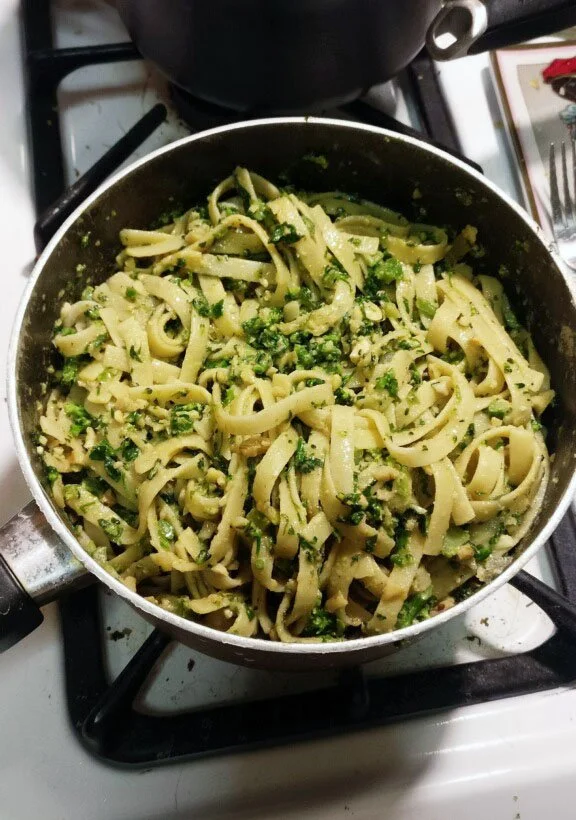 A pan of cooked fettuccine pasta mixed with chopped green herbs on a stovetop.