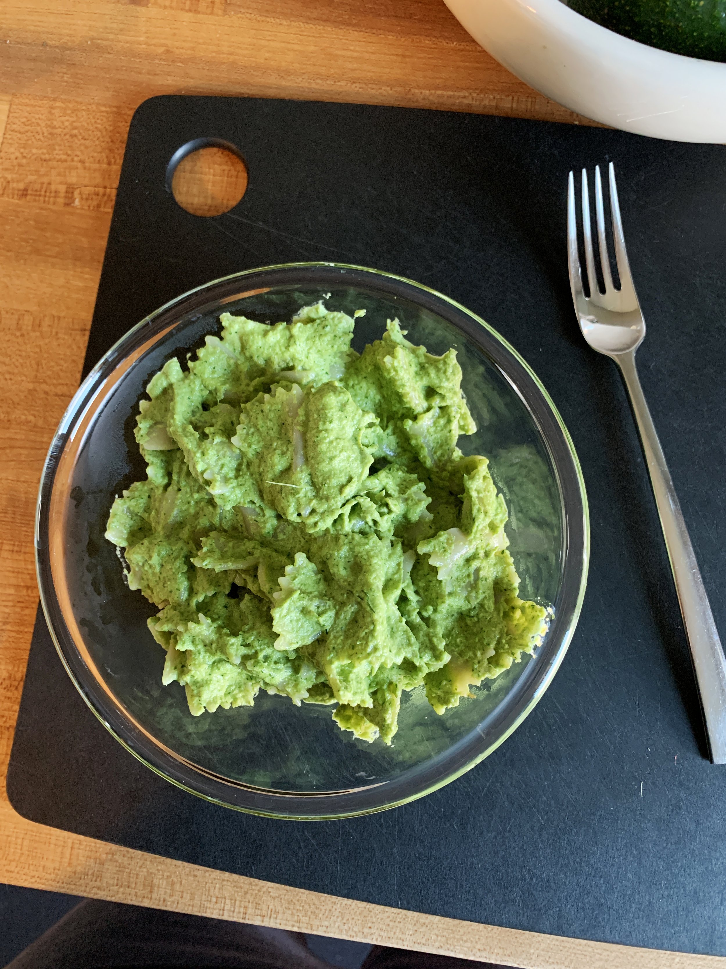 A glass bowl of mashed avocado on a black placemat with a fork nearby.