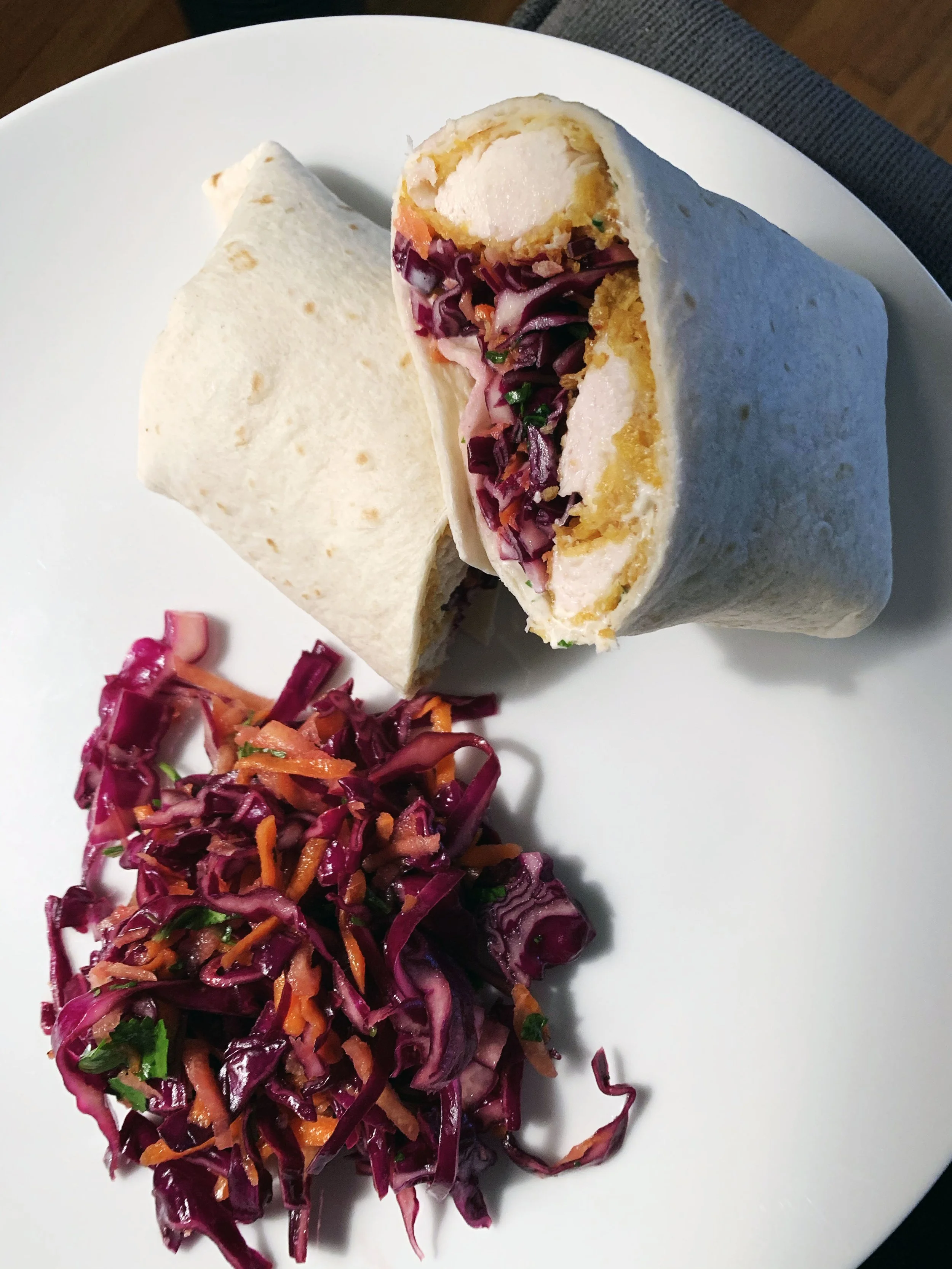 A white plate with a sliced chicken wrap and a side of shredded red cabbage slaw with carrots and herbs.