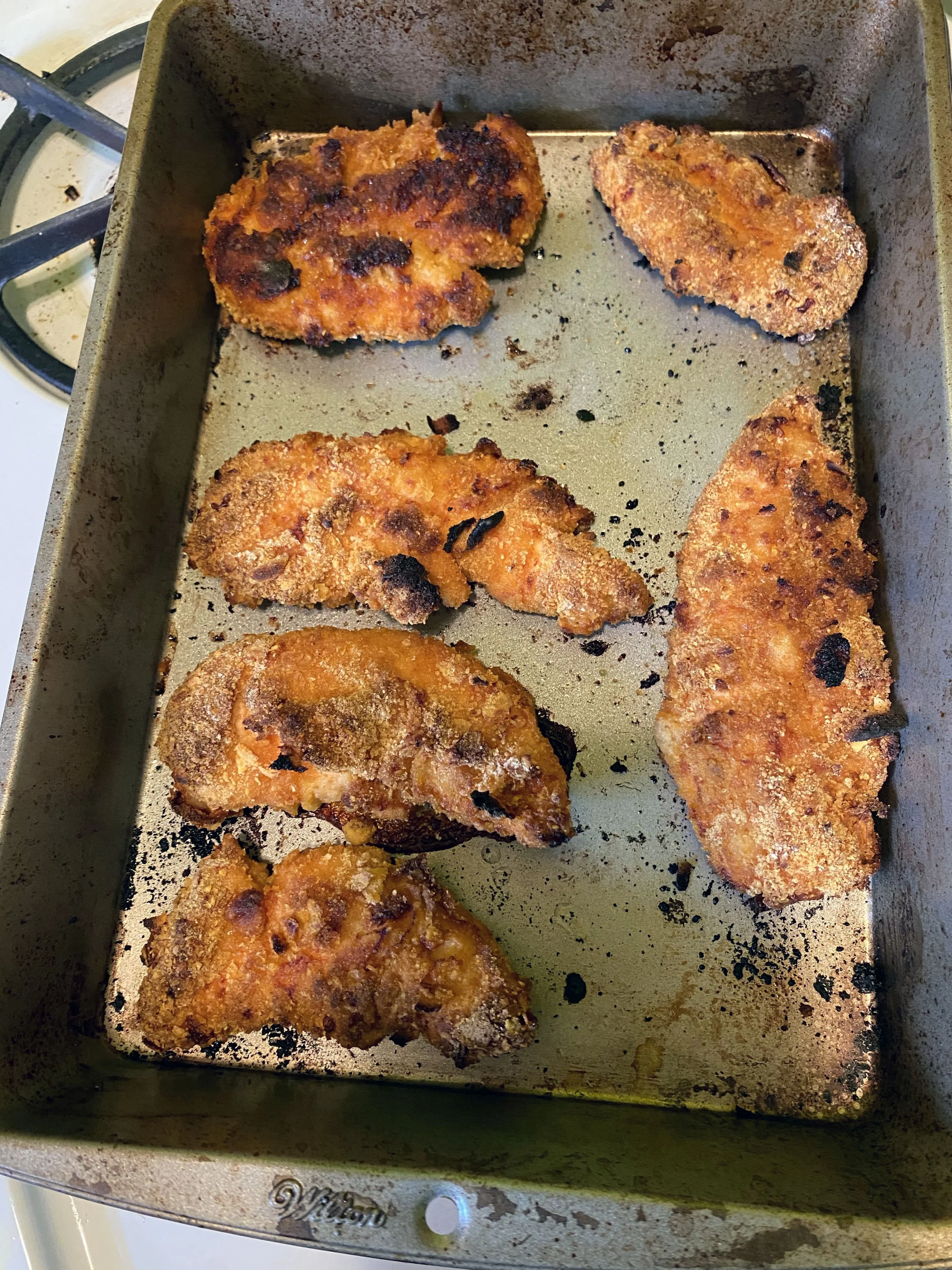 Baked breaded chicken pieces on a baking sheet, some with a crispy, golden-brown crust.