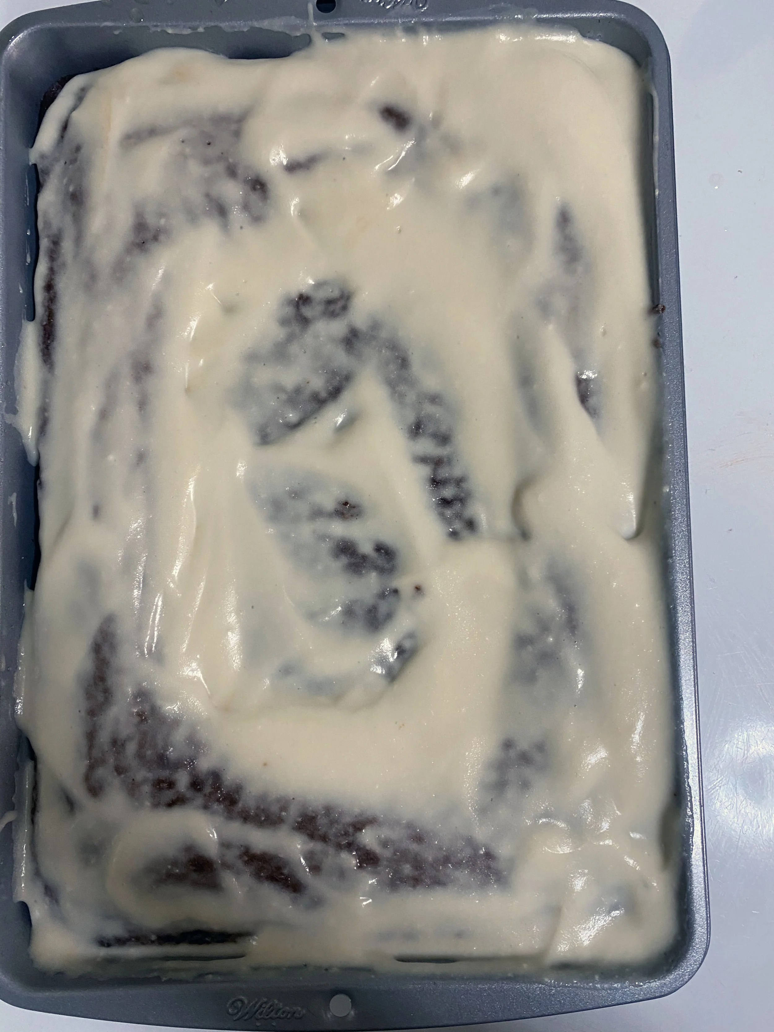 Unbaked cinnamon roll cake with cream cheese frosting in a rectangular pan.