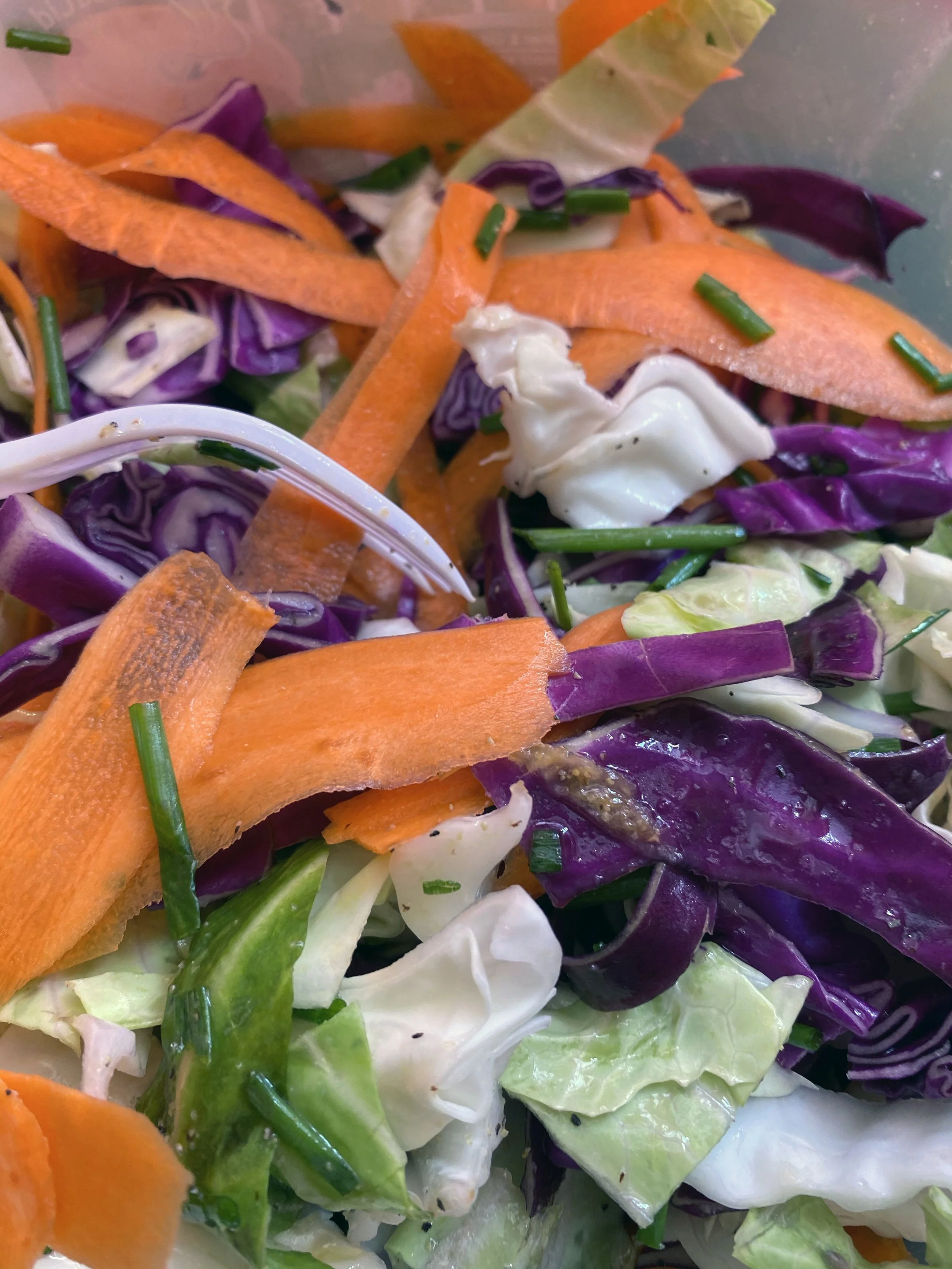 Close-up of a mixed vegetable salad with shredded purple cabbage, grated carrots, chopped green onions, and lettuce.