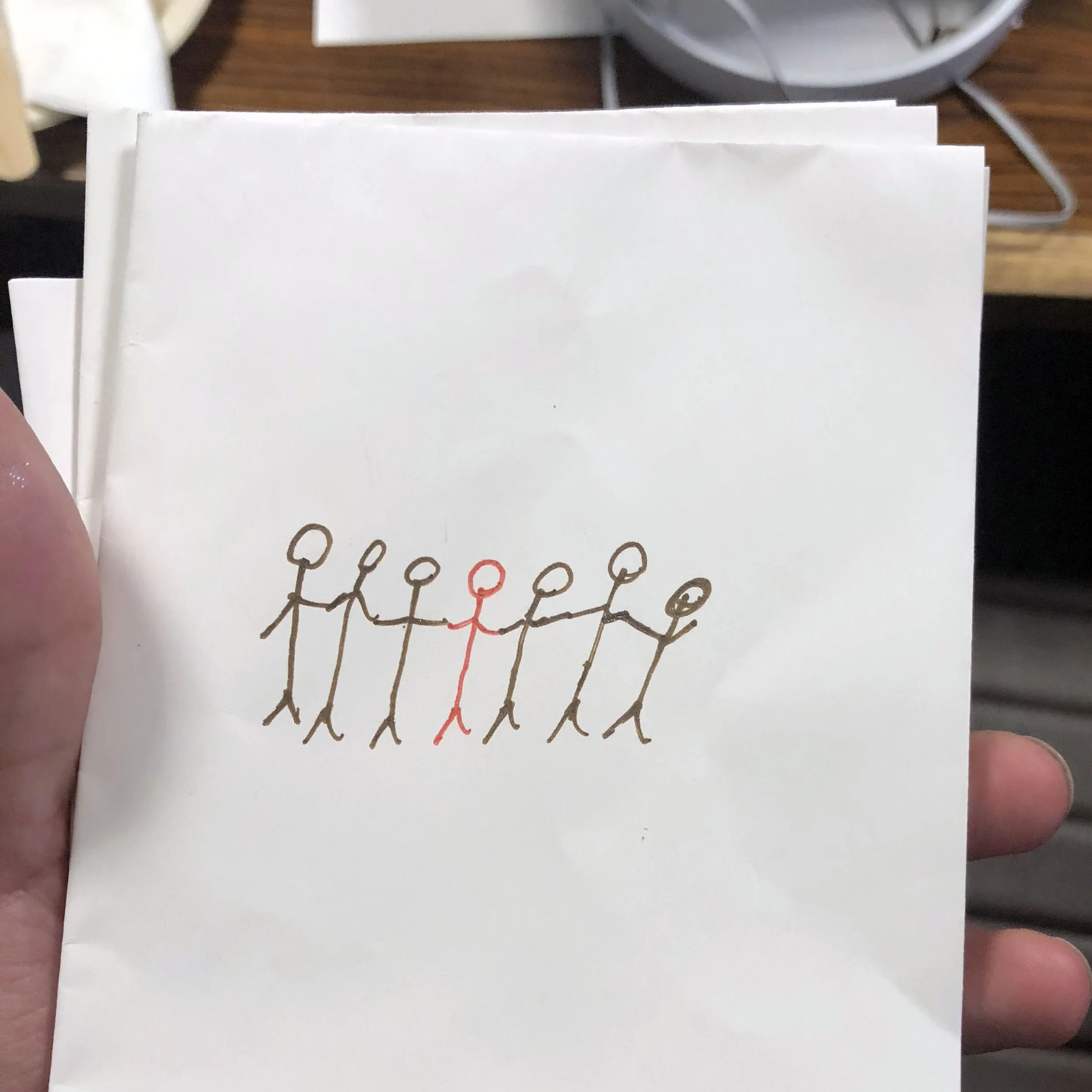Hand-drawn illustration of seven stick figures holding hands, with one in red and the others in black.