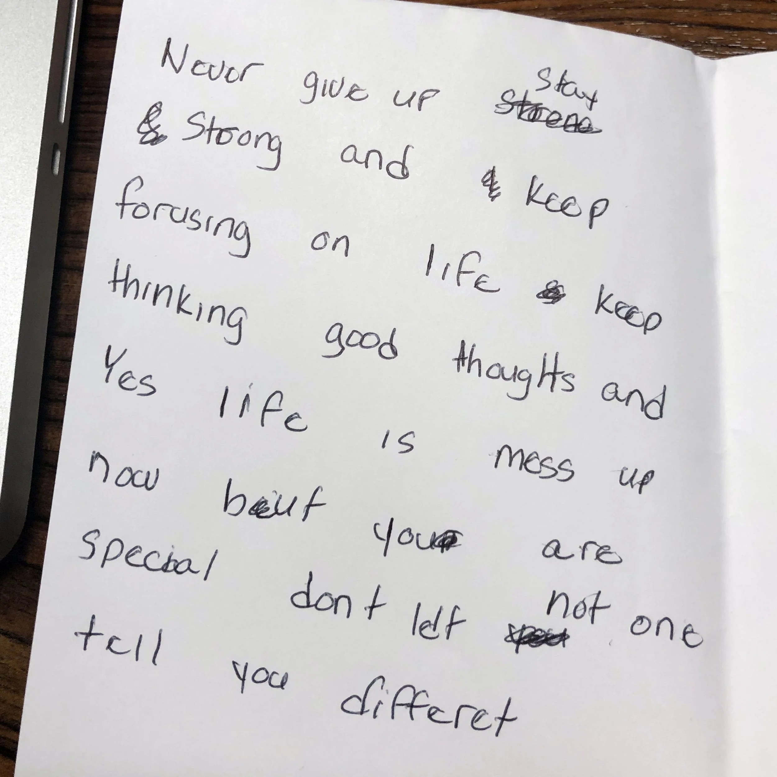 A handwritten motivational quote on a white sheet of paper, with several words crossed out or corrected, emphasizing perseverance and positivity.