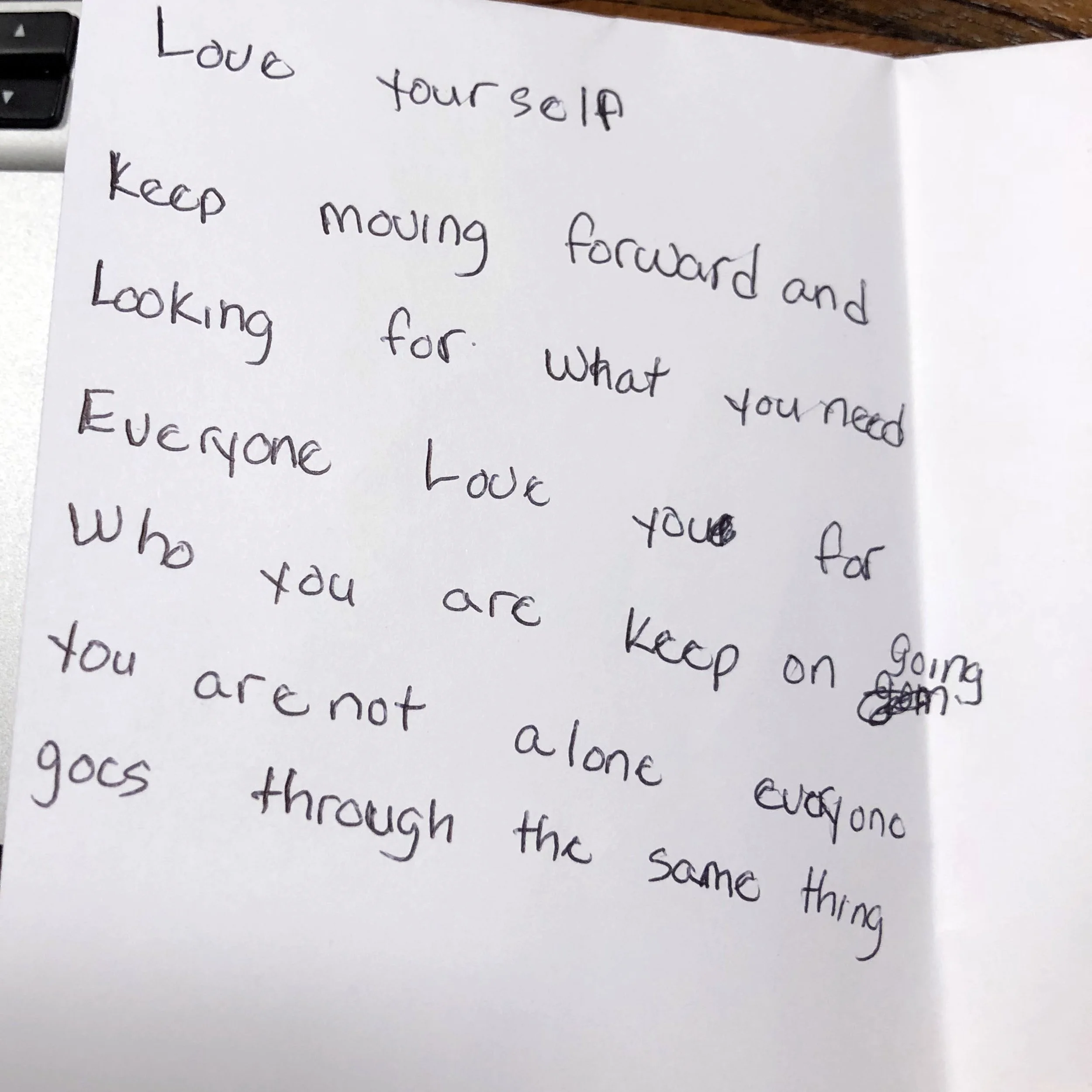 Handwritten motivational note on white paper encouraging self-love, perseverance, and not feeling alone.
