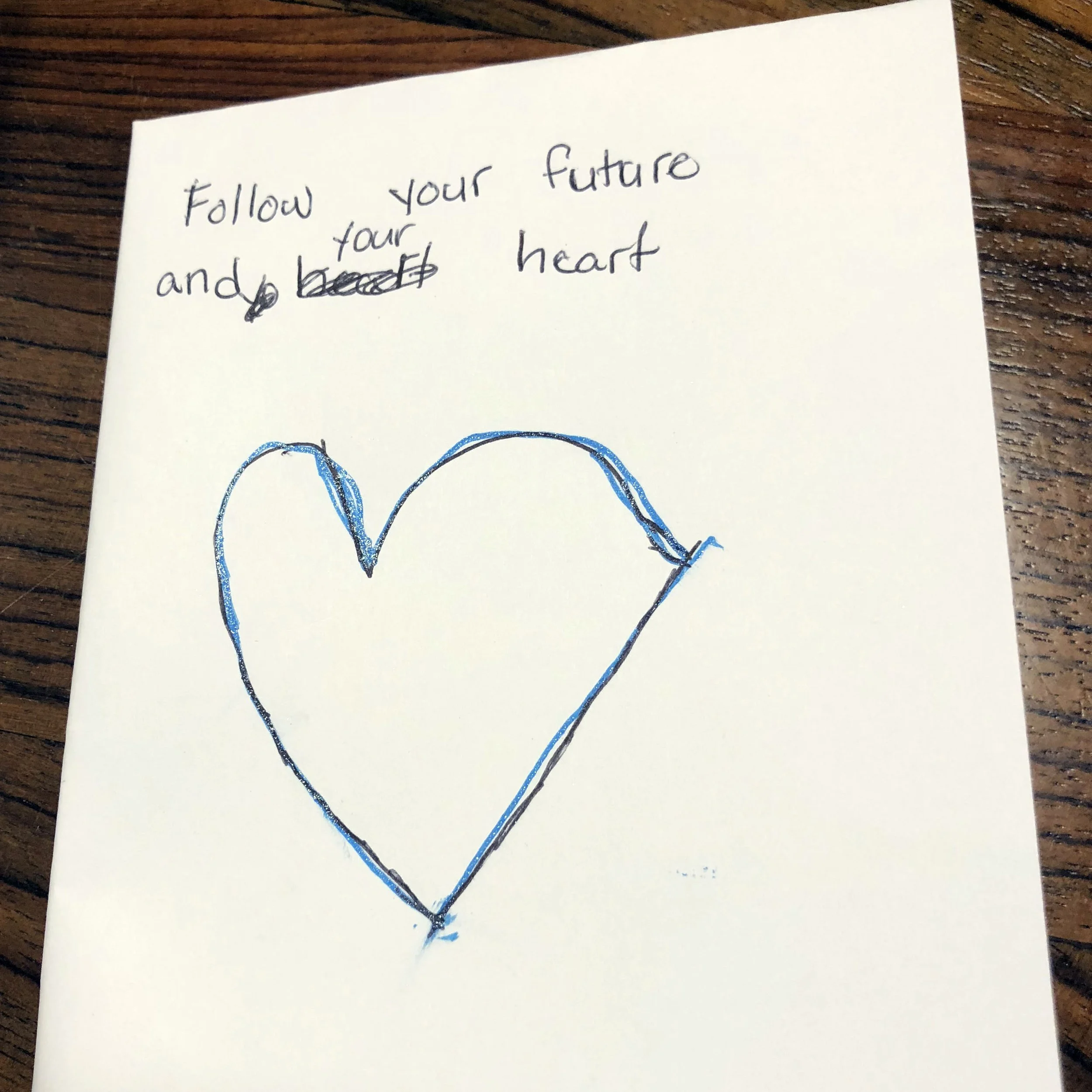 A handwritten note on a piece of paper with a blue heart drawing. The note says, "Follow your future and your heart."
