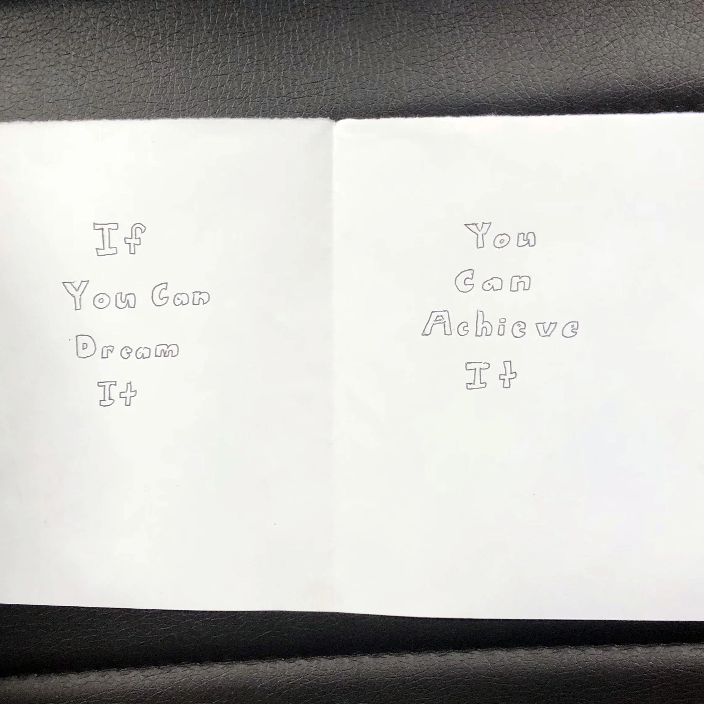 A white paper card with handwritten text on two sides. The left side says, "If You Can Dream It," and the right side says, "You Can Achieve It."