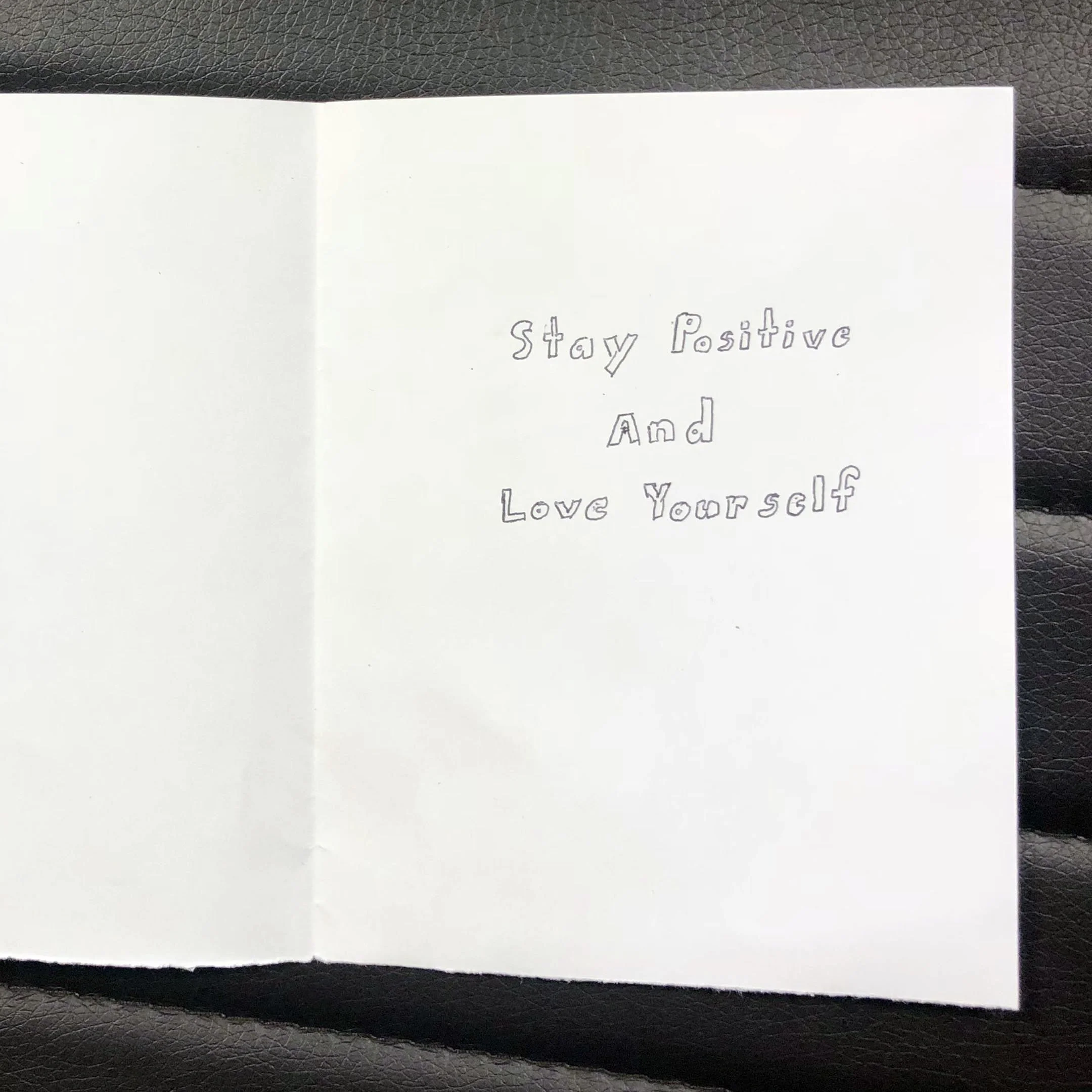 A white card with the handwritten message: 'Stay Positive And Love Yourself'.
