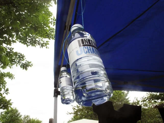 Two large water bottles hanging from a canopy at an outdoor event.