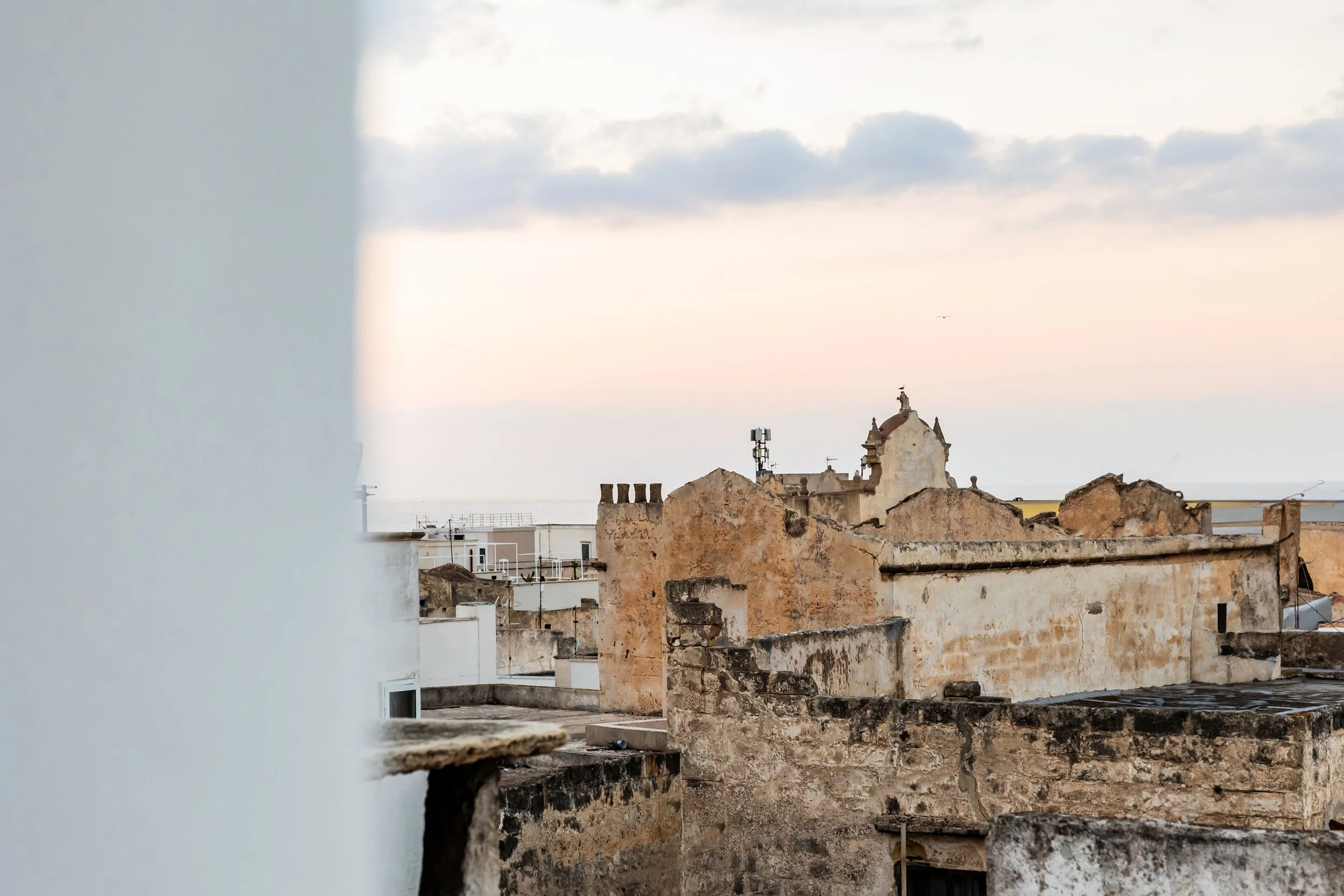 Rooftop view of Gallipoli Old Town, showcasing weathered rooftops, small domes, Mediterranean architecture and soft pastel skies.
