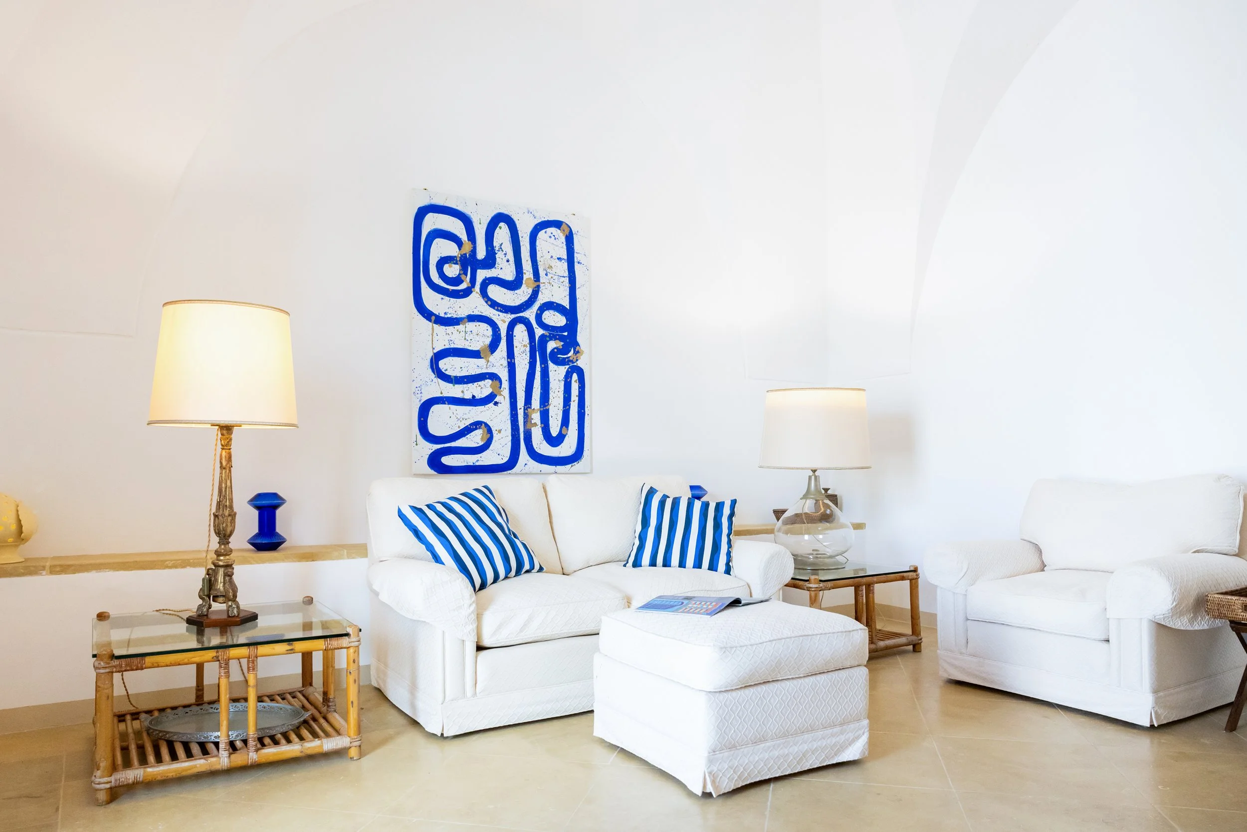 Living room at Palazzo Dolce Vita with star-vaulted ceilings, opening onto the terrace, styled with white sofas, blue accents and abstract artwork.