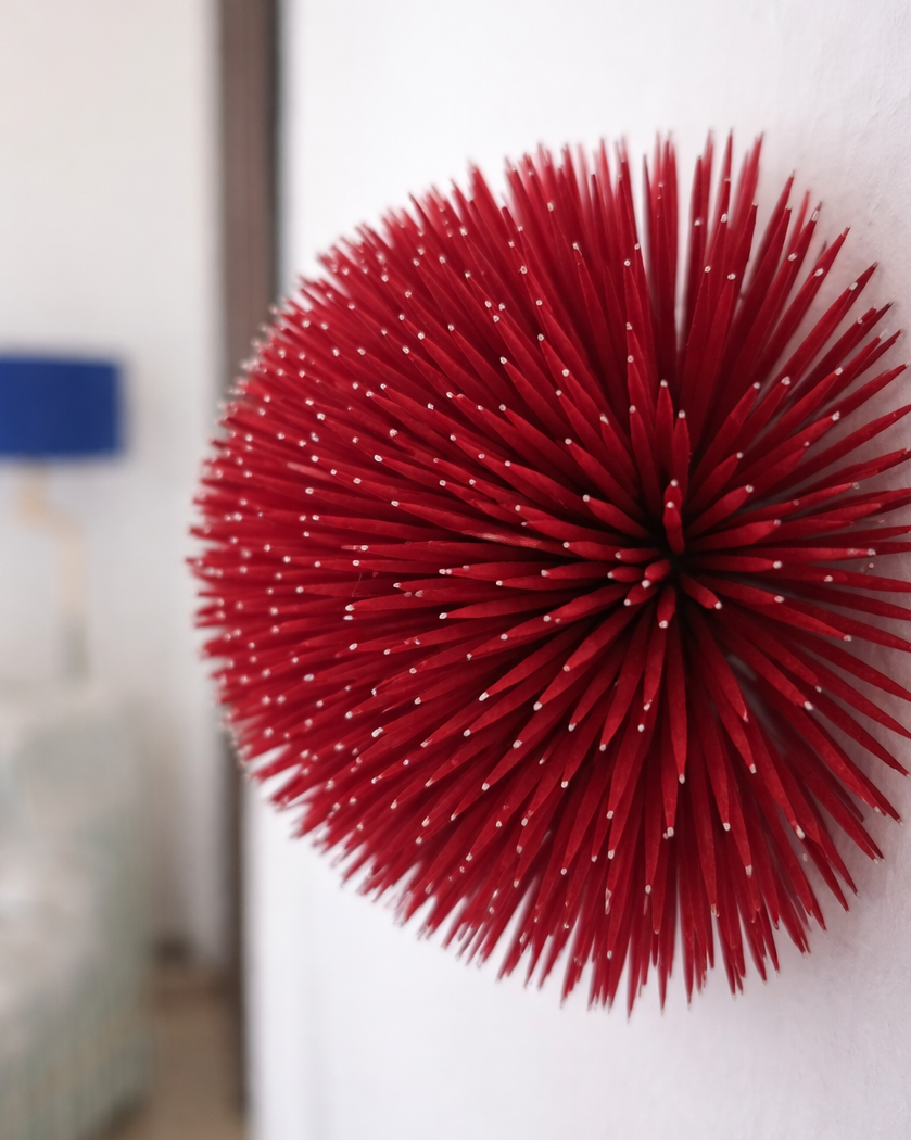 A large red spherical decorative object with numerous thin spikes extending outward, attached to a white wall.