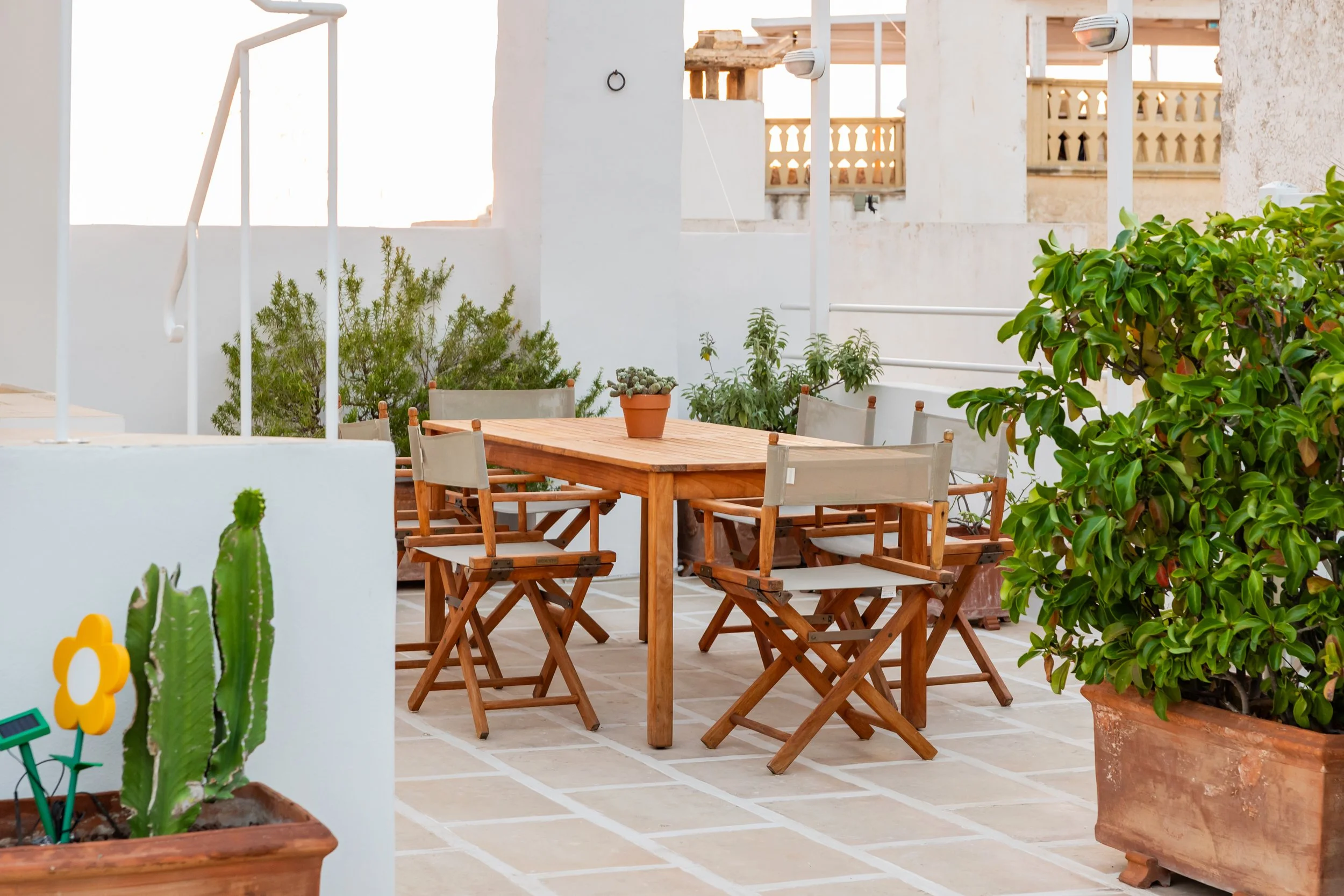 Outdoor kitchen area at Palazzo Dolce Vita, with a teak dining table for six, foldable chairs and potted Mediterranean plants.