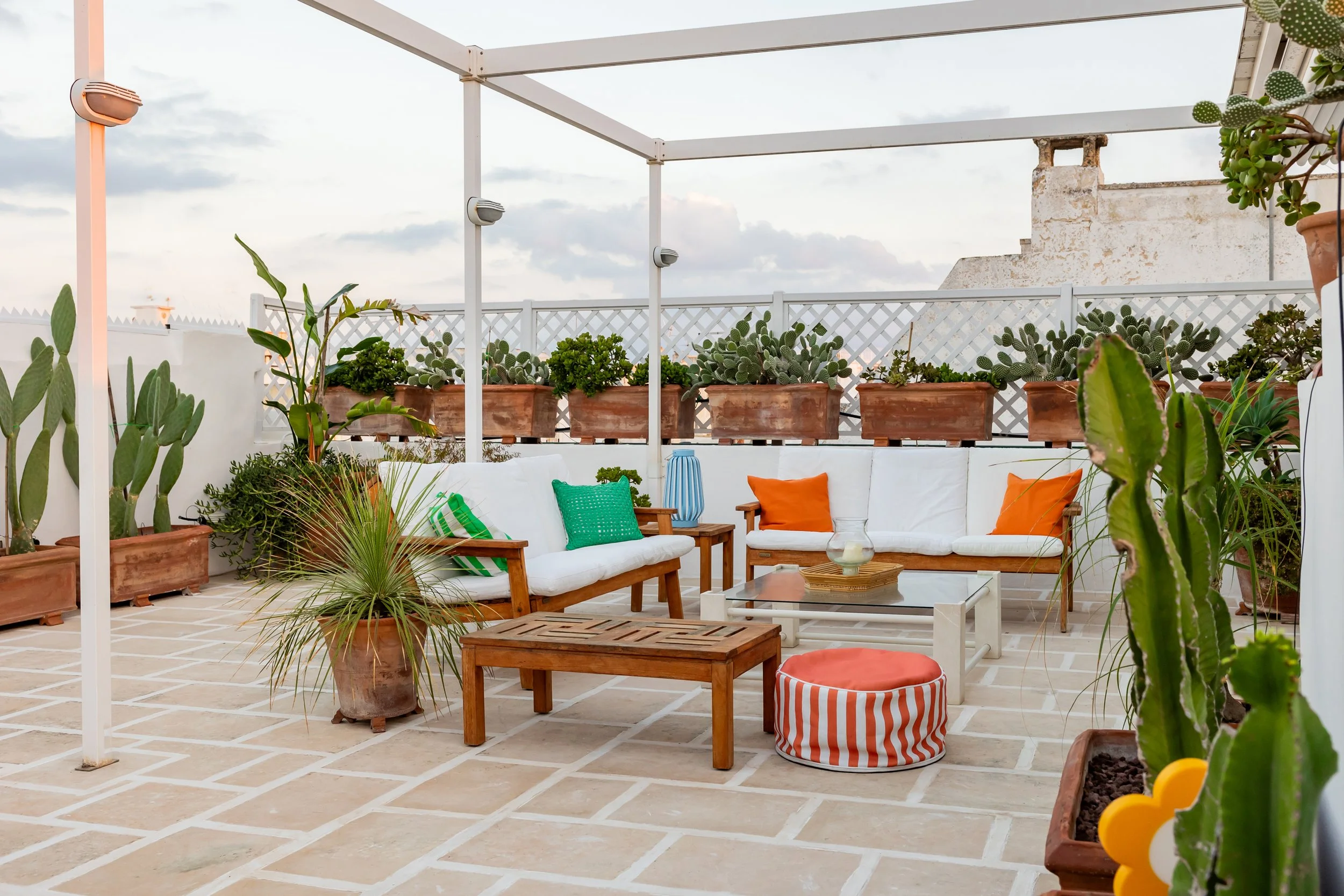 Rooftop outdoor living area at Palazzo Dolce Vita, with cushioned seating, potted cacti and colourful pillows under a changing sky.