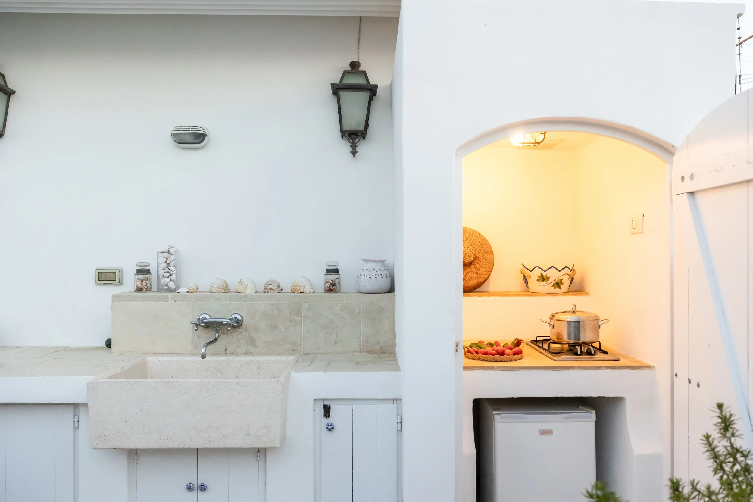 Outdoor kitchen workspace at Palazzo Dolce Vita, with a stone sink, cooking area with stovetop and refrigerator, designed for open-air cooking.
