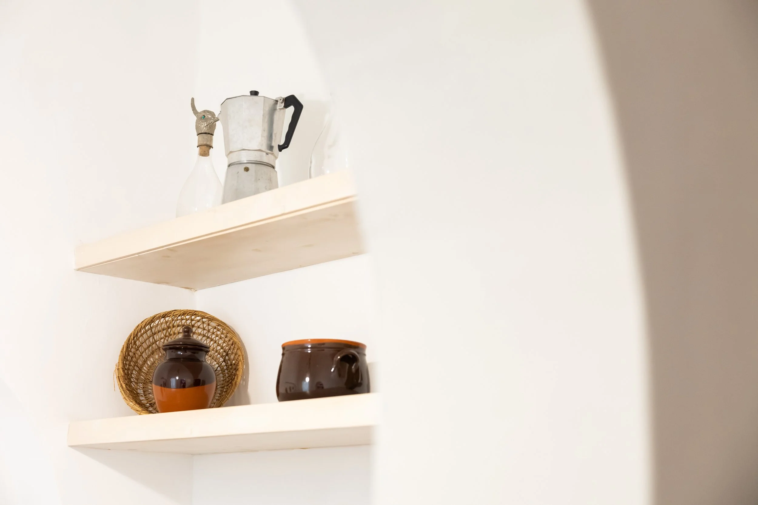 Two white floating shelves with vintage kitchen items, including a coffee pot, glass bottles, and ceramic jars, against a white wall.