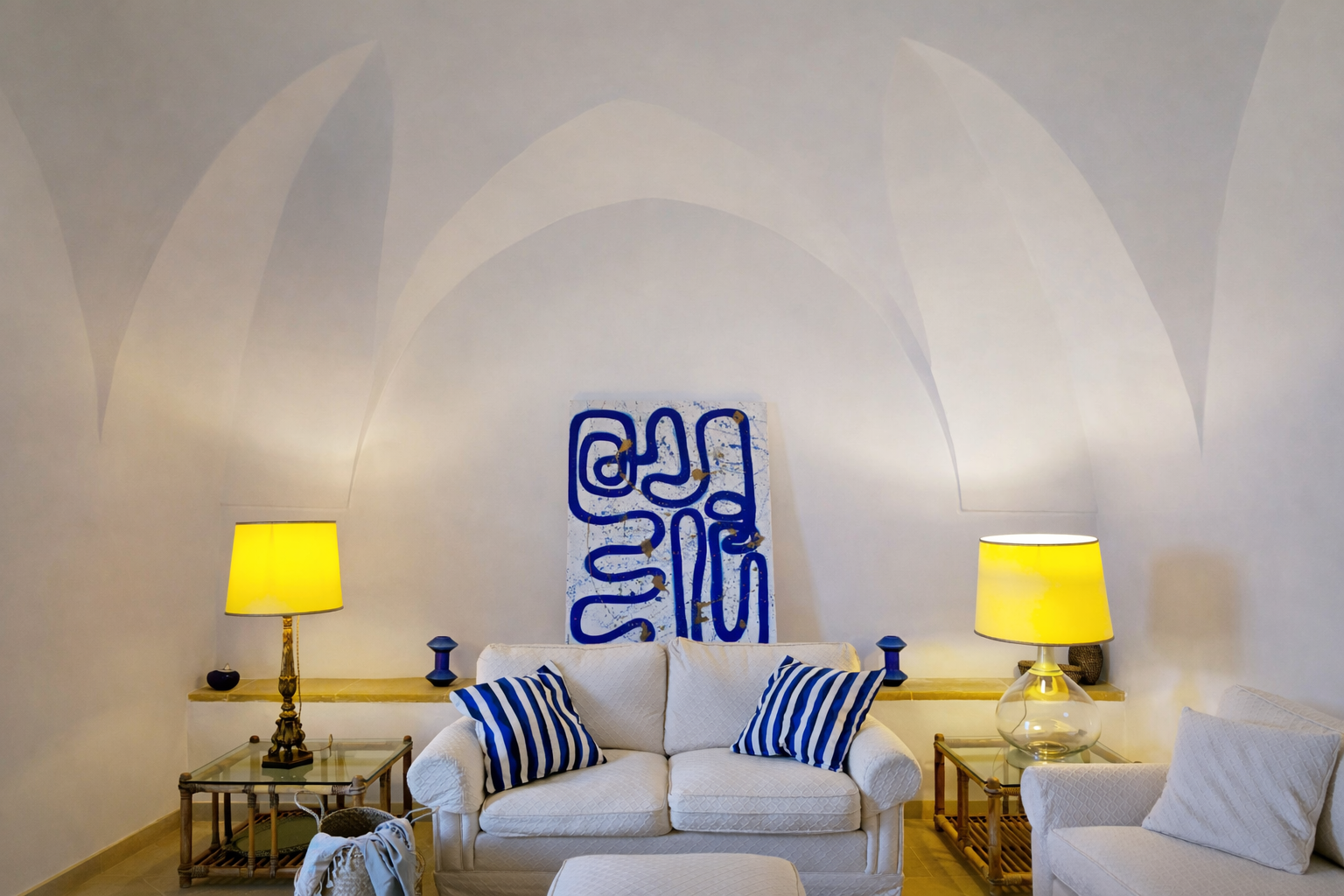 Living room with white sofa, blue and white striped pillows, two yellow lamps, artwork with blue abstract design on the wall.