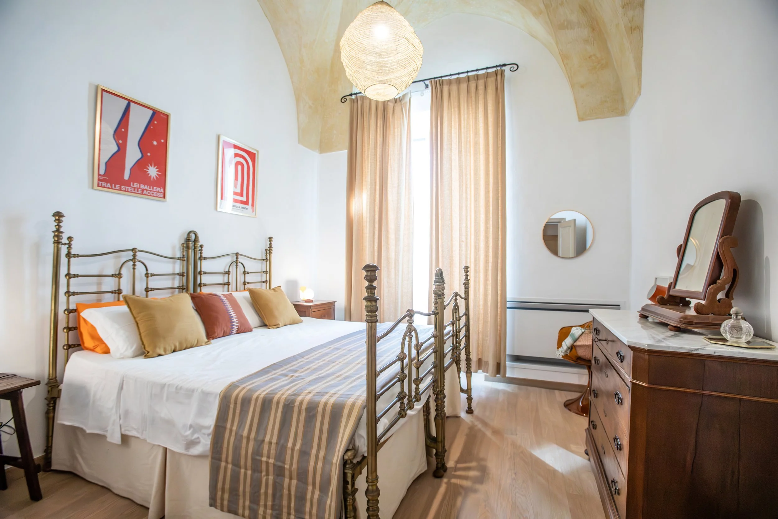 Bright master bedroom at Palazzo Dolce Vita, featuring a brass bed, soft textiles, wooden furniture and a calm, light-filled atmosphere.