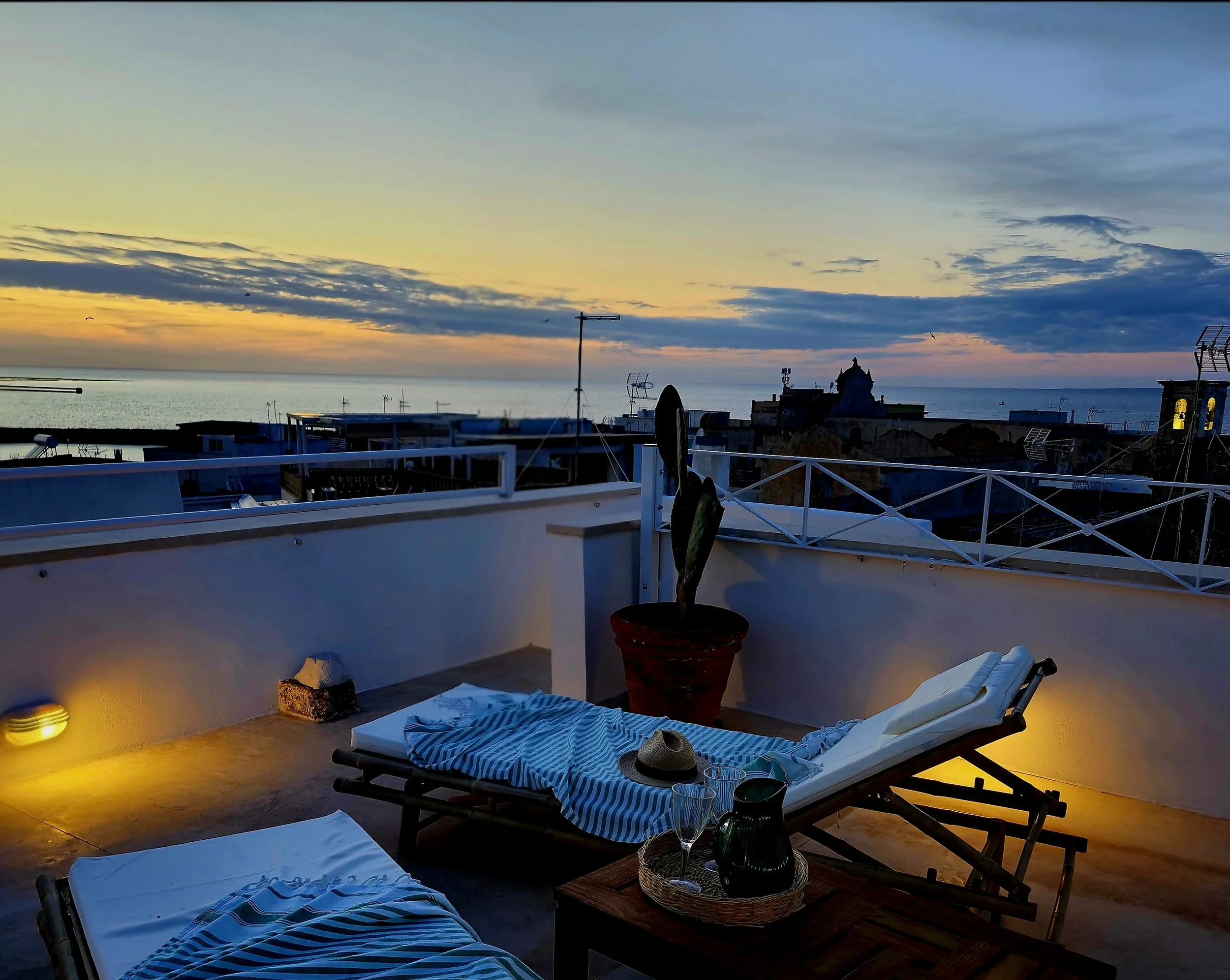Sunset moment on the rooftop terrace of Palazzo Dolce Vita, with lounge seating, cactus plants and panoramic sea views.