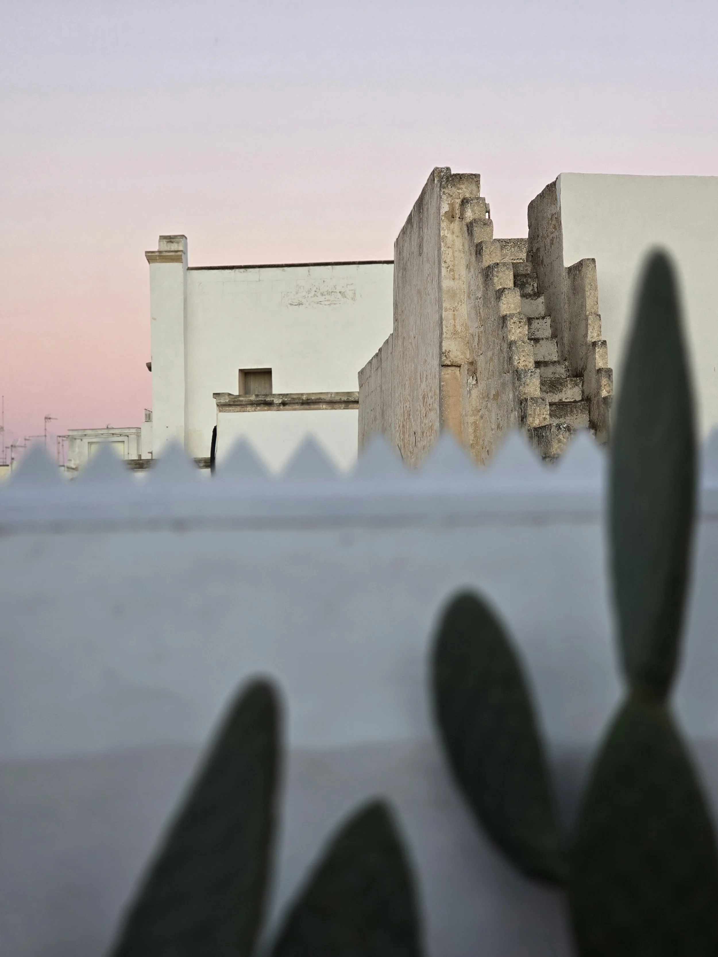 Outdoor living area at Palazzo Dolce Vita, with white architecture and open views under a soft pink and blue sky.