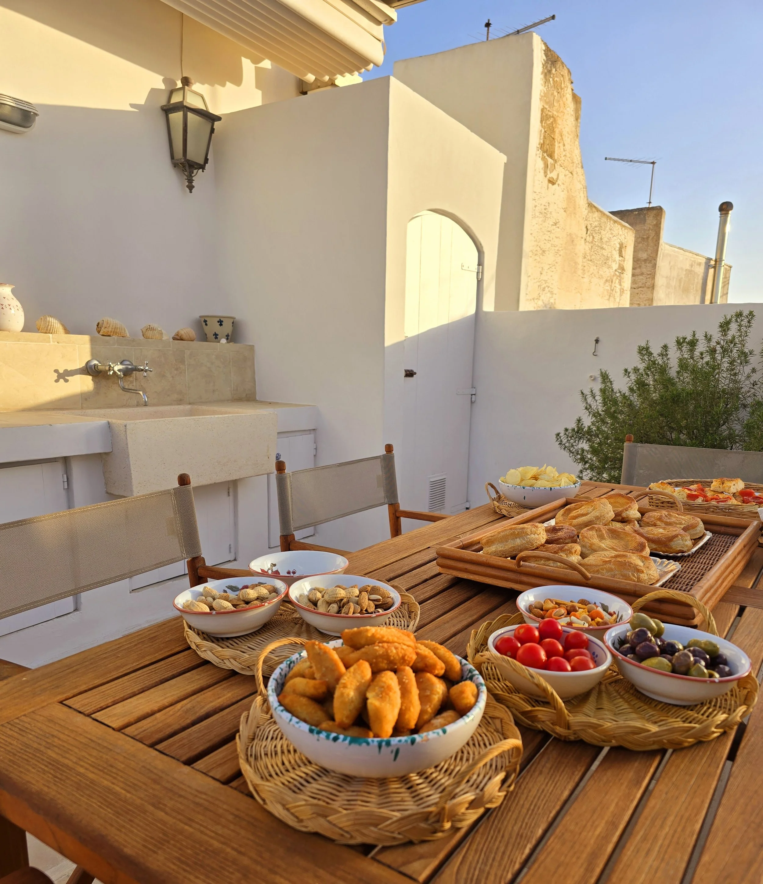 Shared aperitivo during golden hour in the outdoor kitchen at Palazzo Dolce Vita, with bread, olives, cherry tomatoes and snacks enjoyed together in warm sunset light.
