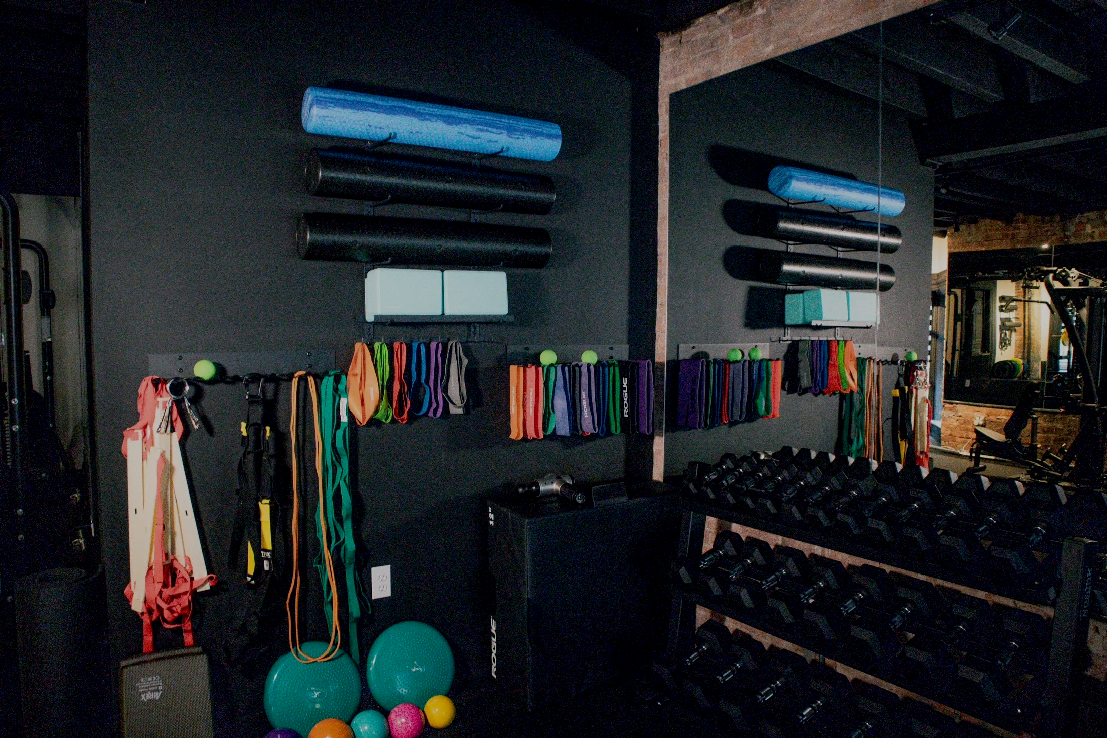 Gym corner with exercise equipment, weights, resistance bands, medicine balls, foam rollers, and mirrors.