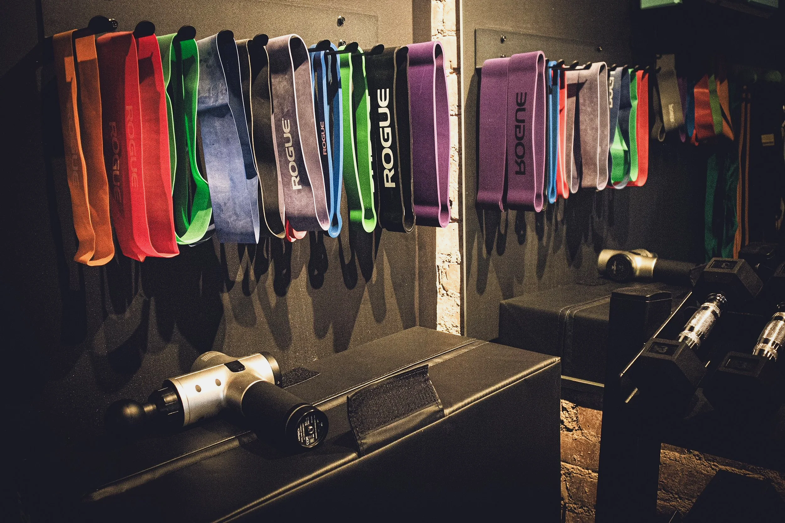 Colorful resistance bands hanging on a black wall with workout equipment below.