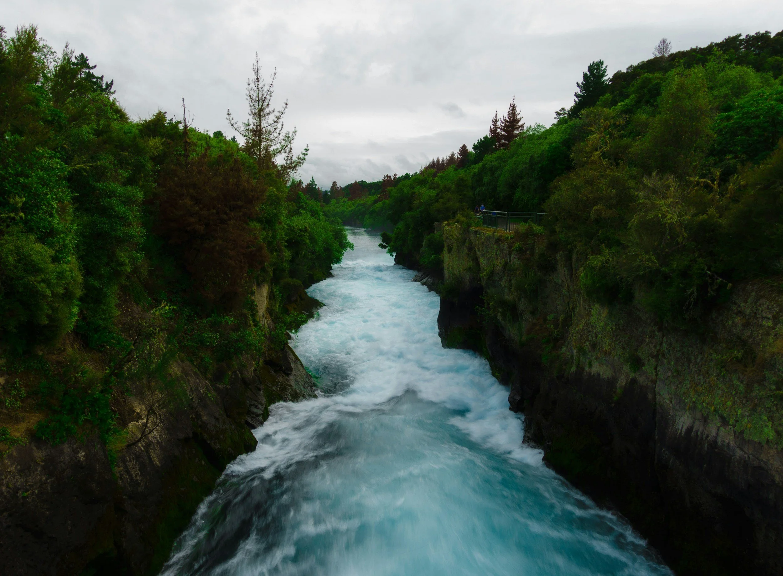 A river flowing between green forested hills with cloudy sky overhead.