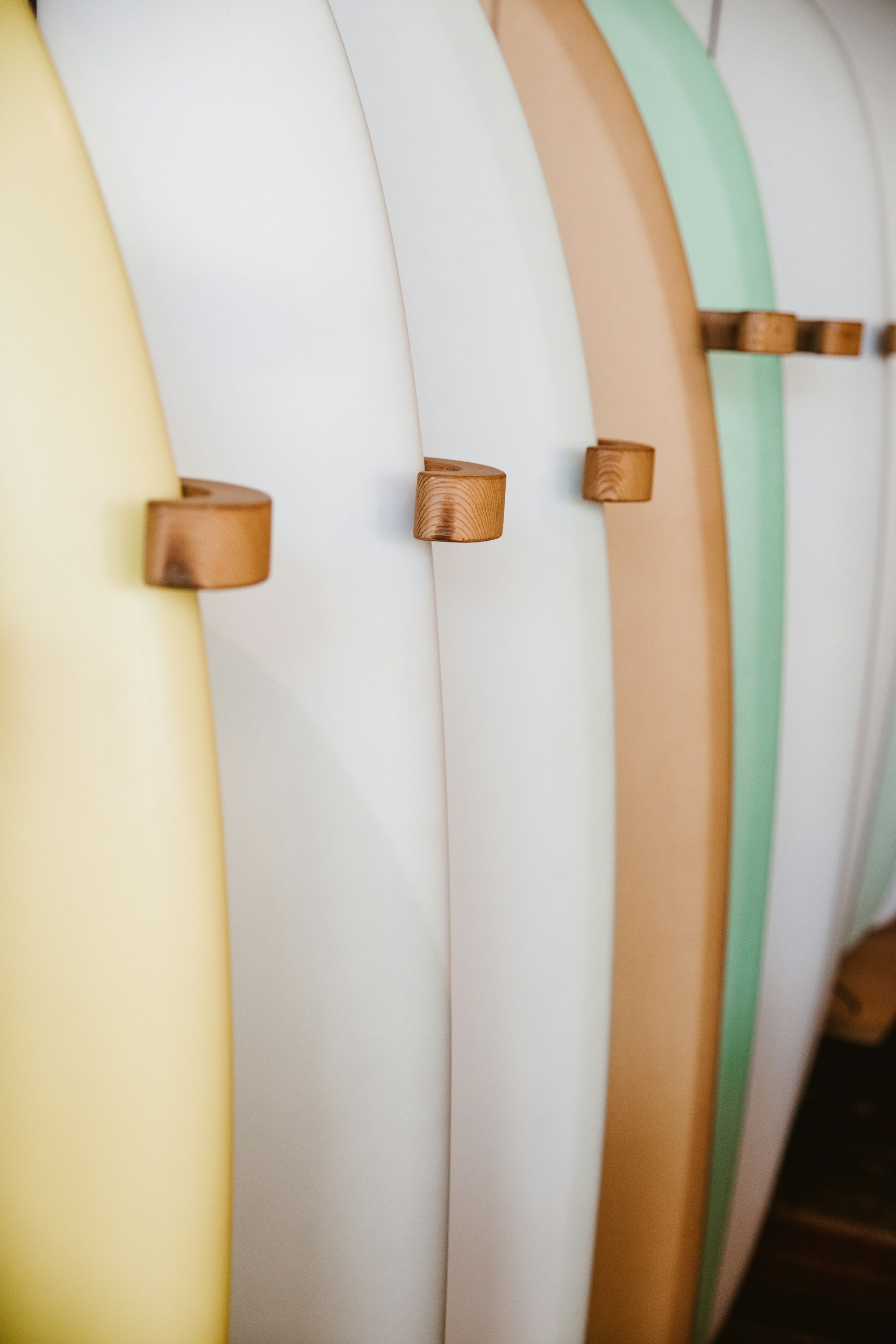 Close-up of colorful, pastel-colored surfboards with wooden hooks mounted on each for hanging.