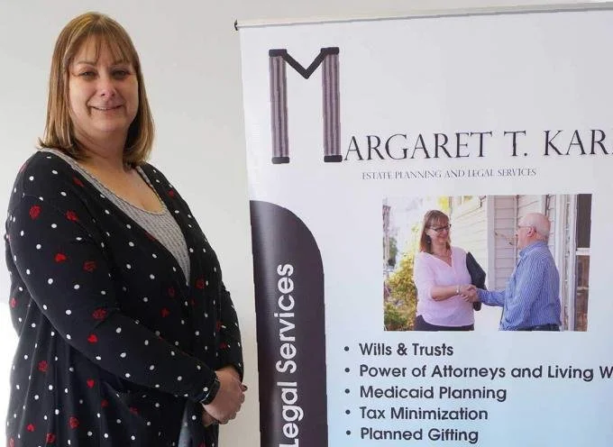 Estate planning attorney Margaret T. Karl standing beside a banner listing legal services including wills, trusts, and Medicaid planning