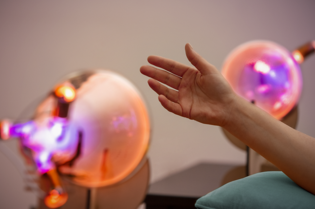A person's hand reaching towards a colorful, glowing plasma ball on a table.