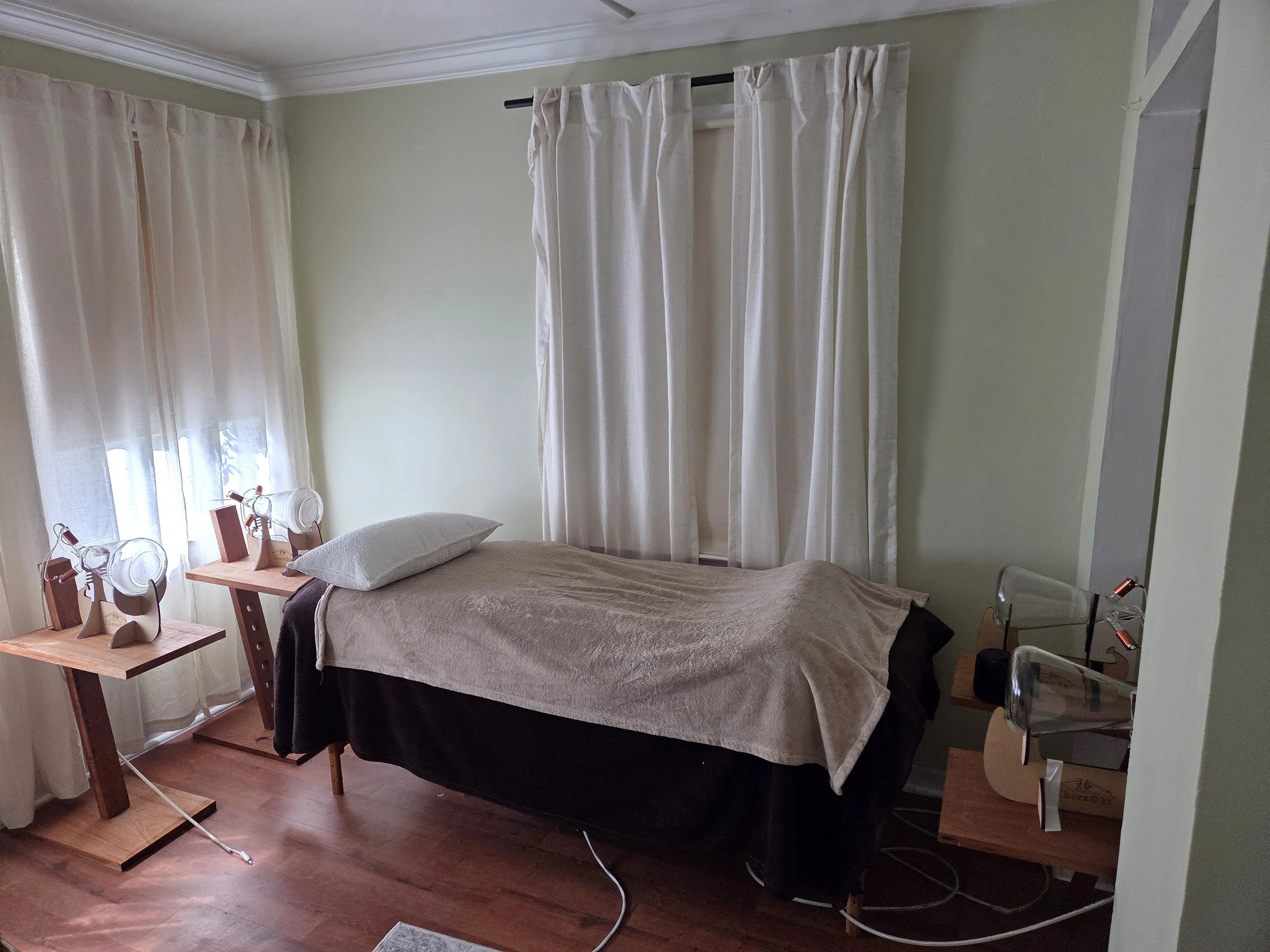 A bedroom with a bed, two wooden side tables, and two modern lamps, curtains covering windows, and hardwood flooring.