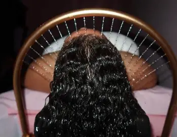 Person lying face down on a bed, their head resting on a pillow, seen through a decorative mirror with a circular, bead-adorned frame