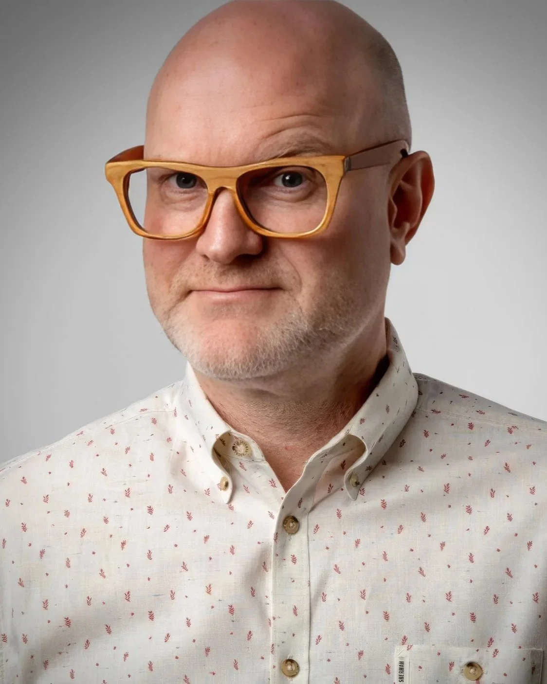 Christopher Owens, a strategist and educator with glasses and a short beard, wearing a light-colored button-down shirt with small red patterns, looking at the camera against a plain gray background.