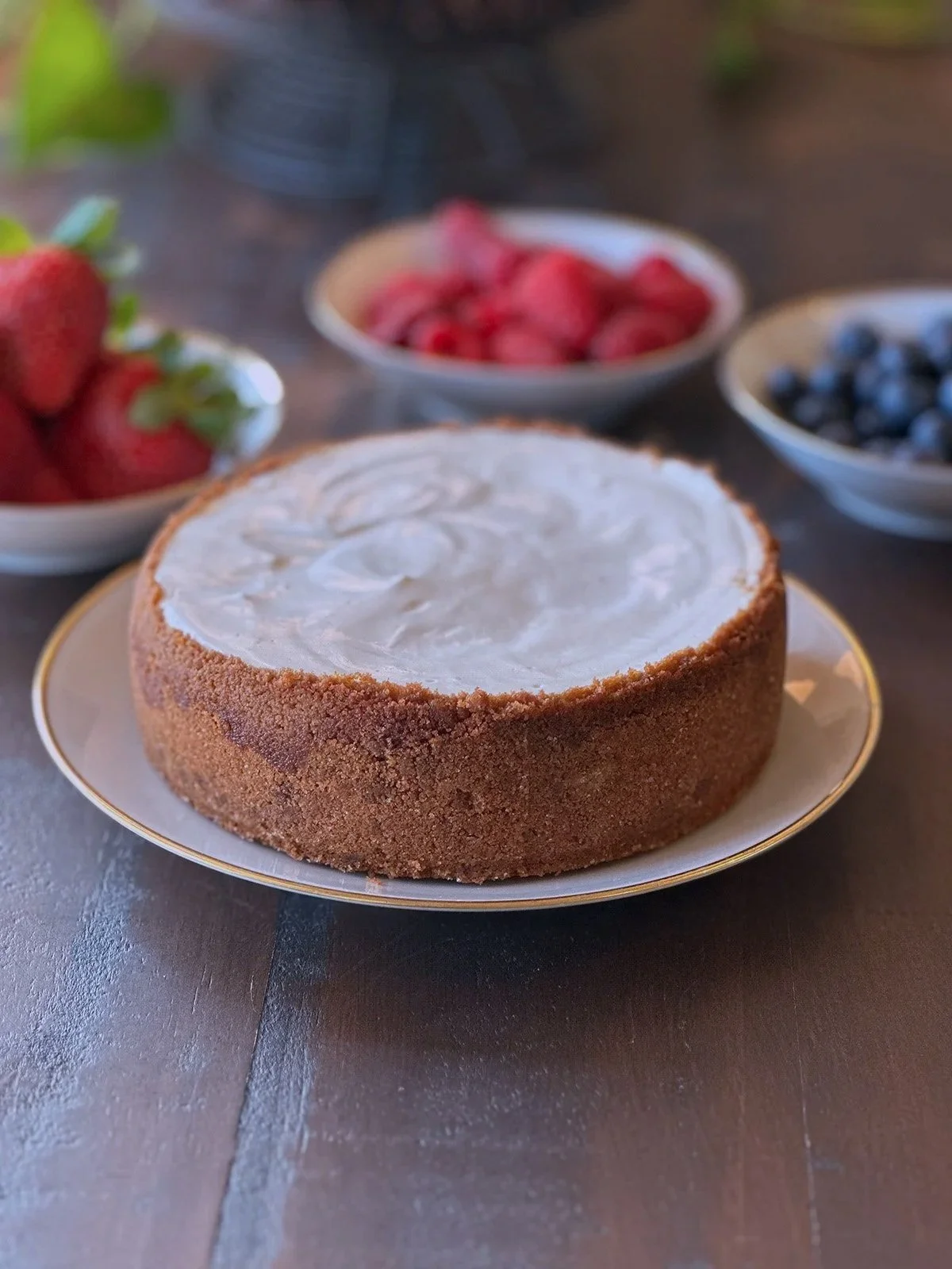 Cheesecake with graham cracker crust with bowls of blueberries raspberries and strawberries