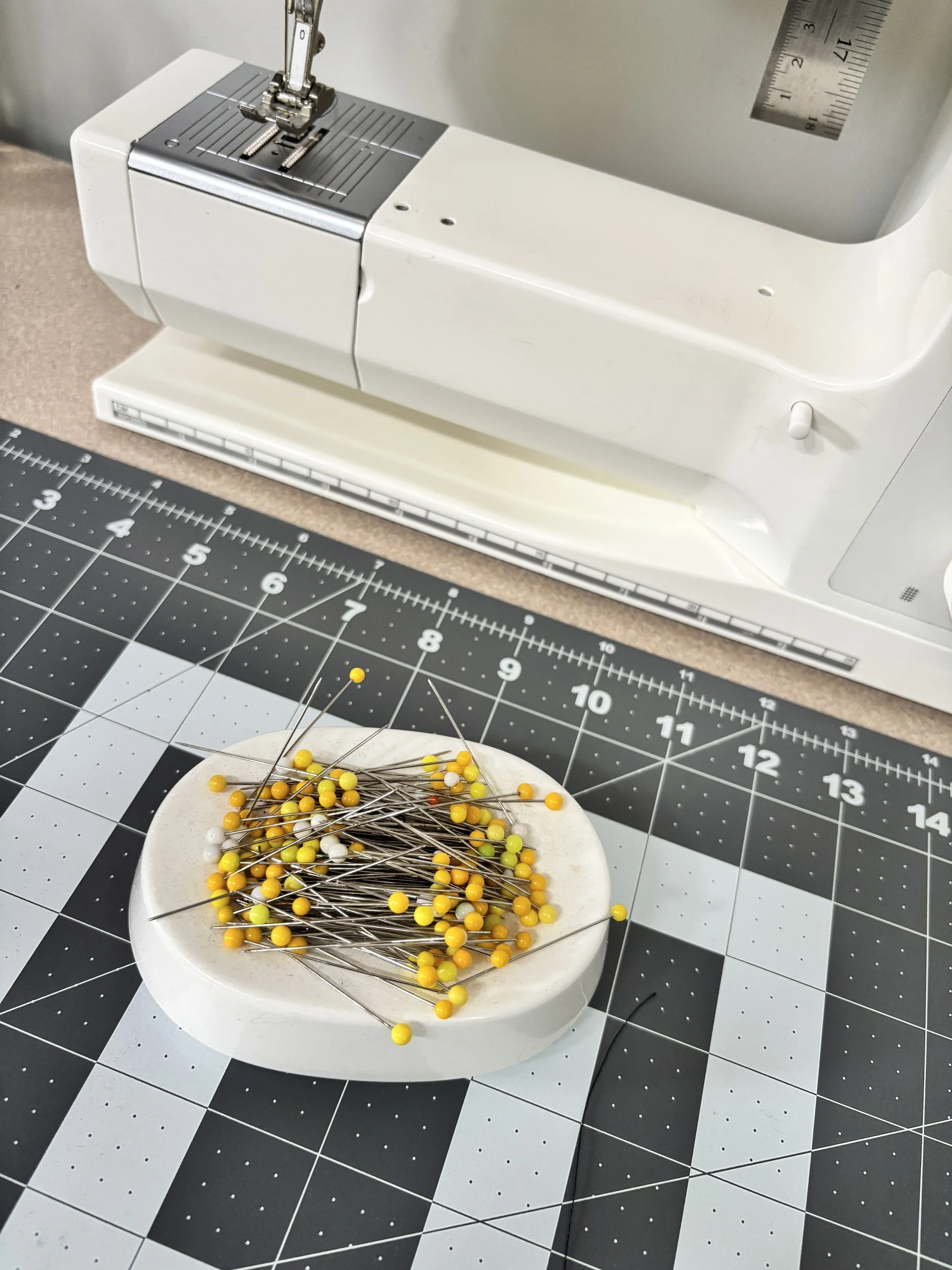 A sewing machine, a cutting mat with measuring grid, and a magnetic pin cushion with straight pins used to teach sewing and learn to sew.