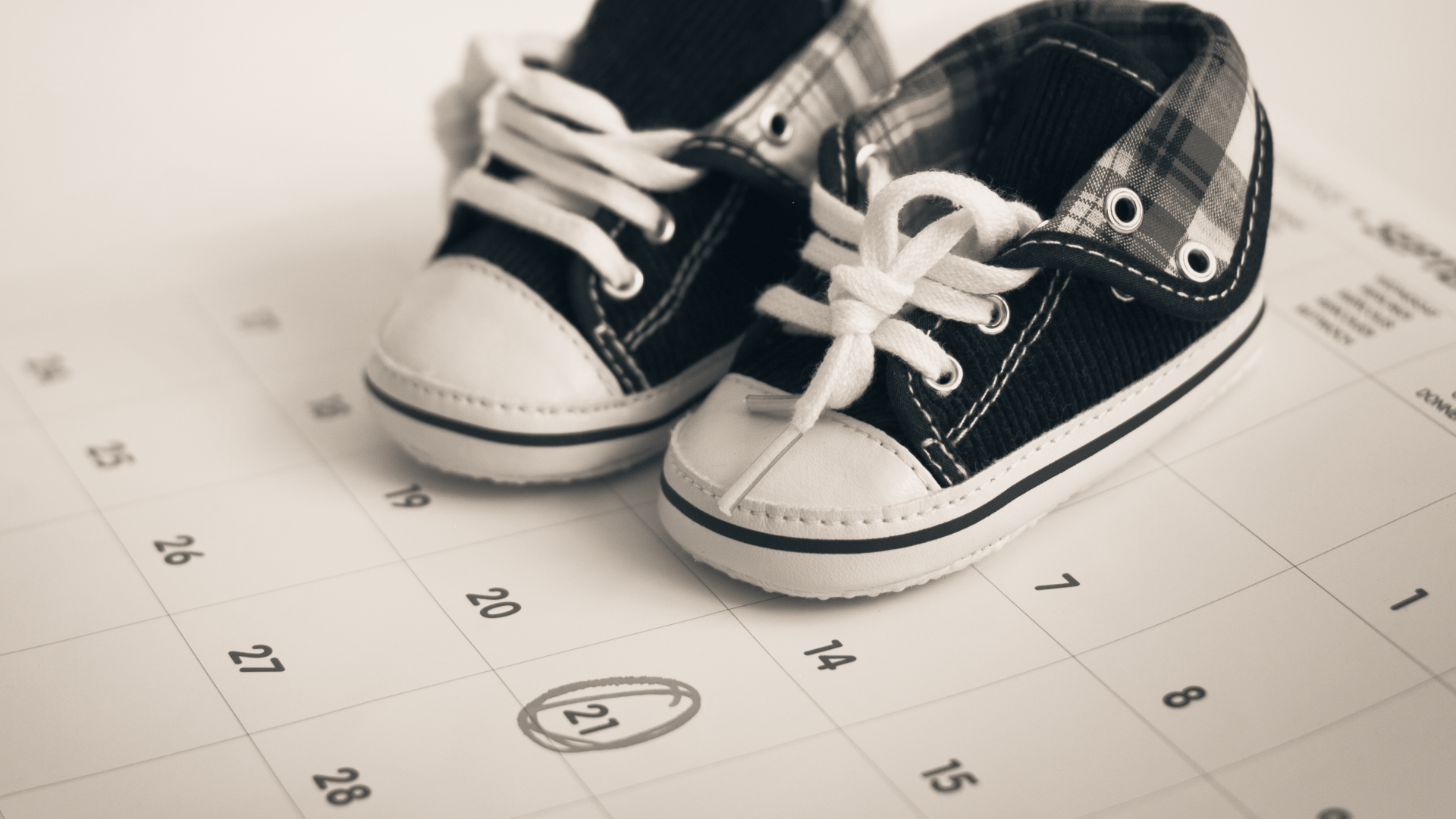 Pair of small black and white baby shoes placed on a calendar with the date 18 circled.