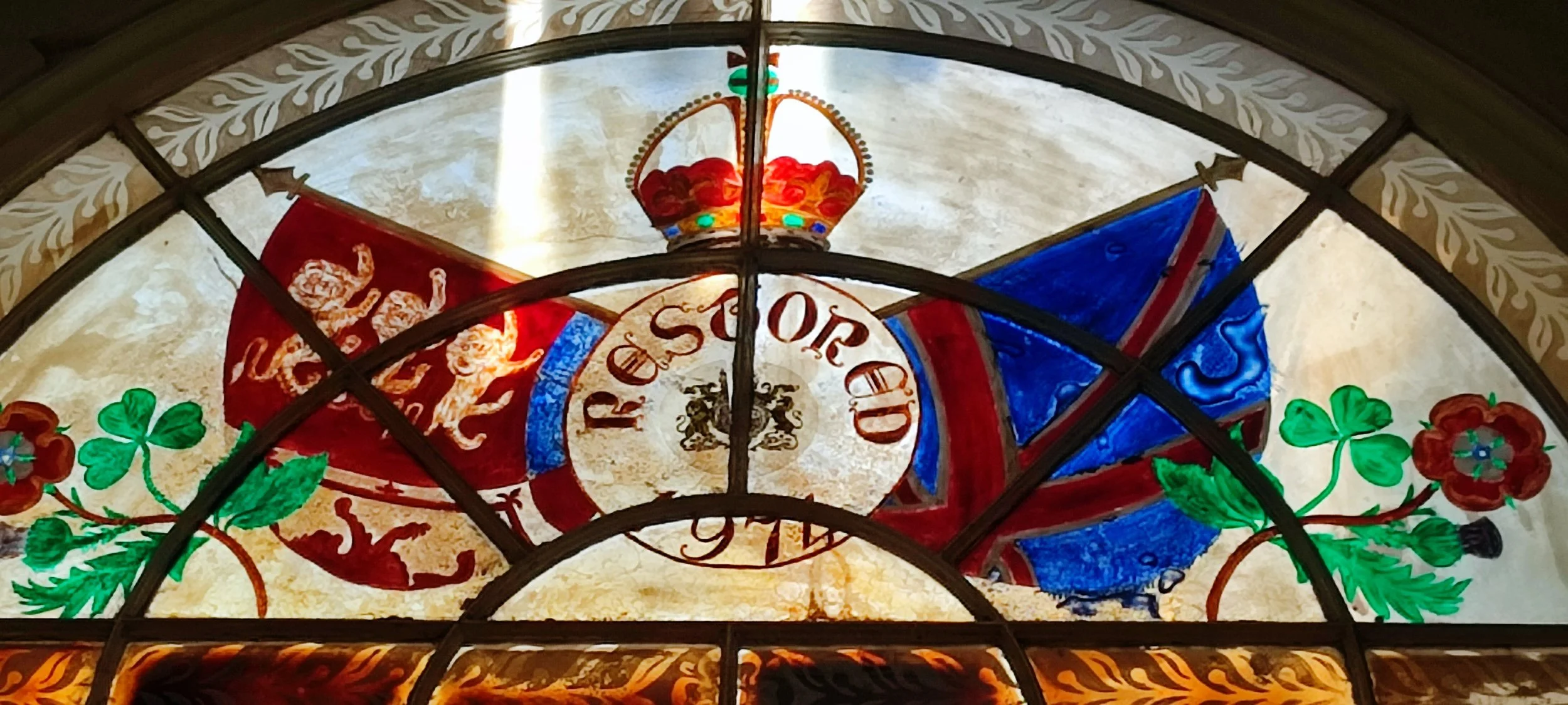 Decorative stained glass with a crown, a Union Jack represented by red, white, and blue colors, a red banner with a lion and crown, the words "Respect of the" inside a circular emblem, red and green floral motifs, and ornate gold accents at the bottom.