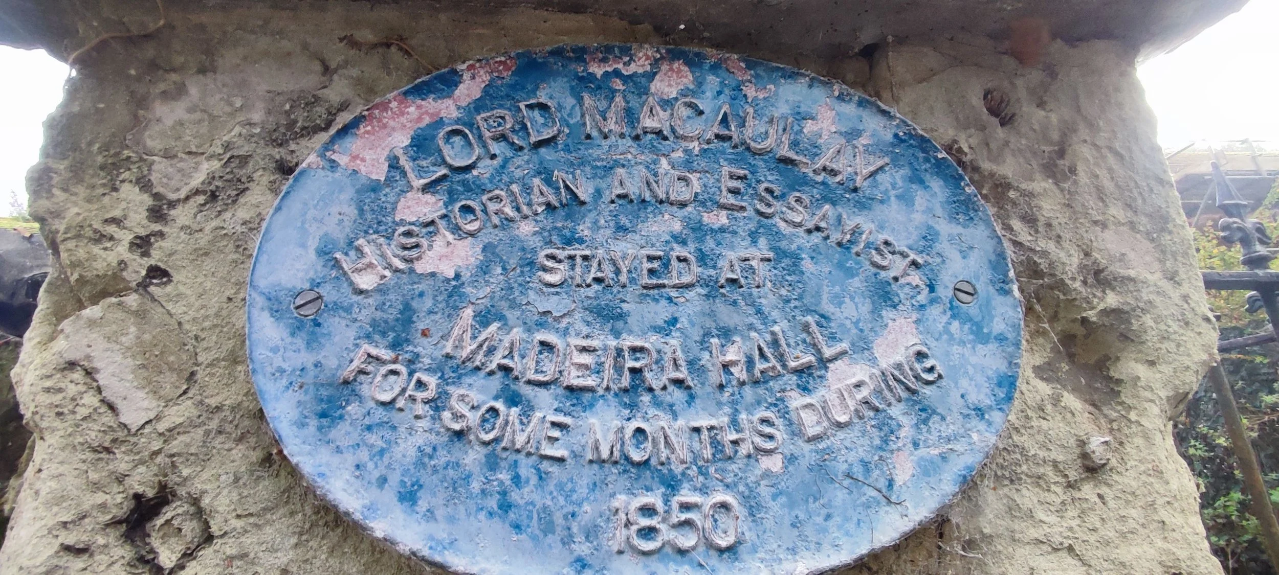 Historical blue metal plaque mounted on stone wall, reading: 'Lord Macaulay historian and essayist stayed at Midera Hall for some months during 1850.'