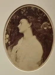 A vintage sepia-toned portrait of a woman in profile, framed oval, outdoors with trees in the background.