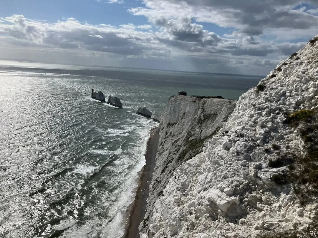Cliffside view overlooking the ocean with white chalk cliffs, rocks in the water, and a cloudy sky.