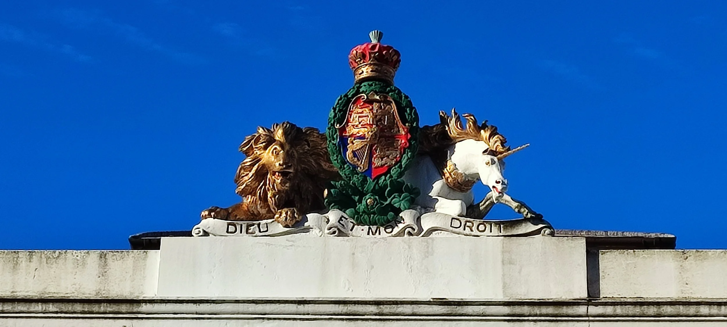 A decorative crest featuring a lion and a unicorn, with a colorful shield and a crown, on top of a building against a blue sky.