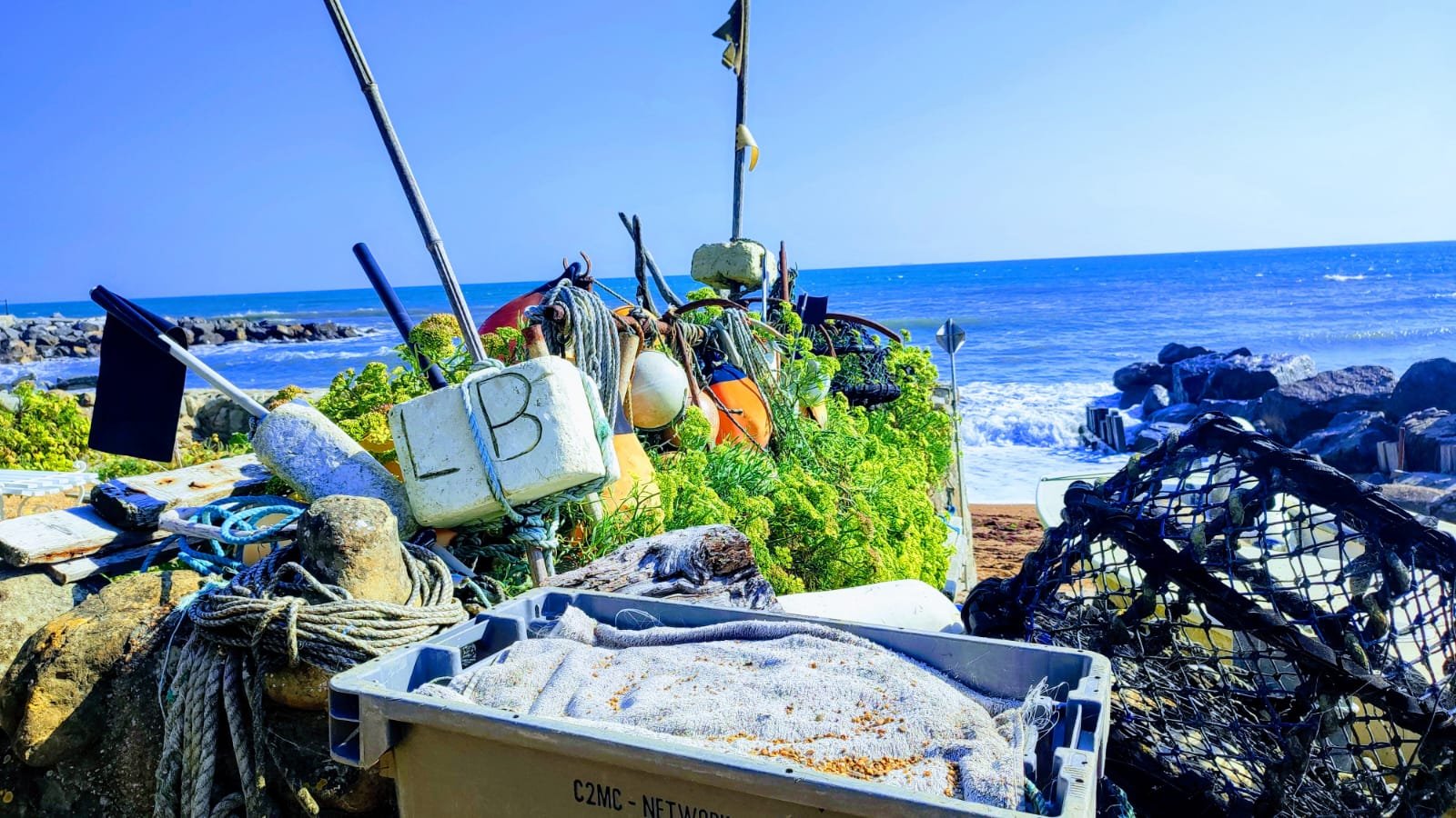 Seaweed and fishing equipment on a rocky beach with ocean waves in the background.