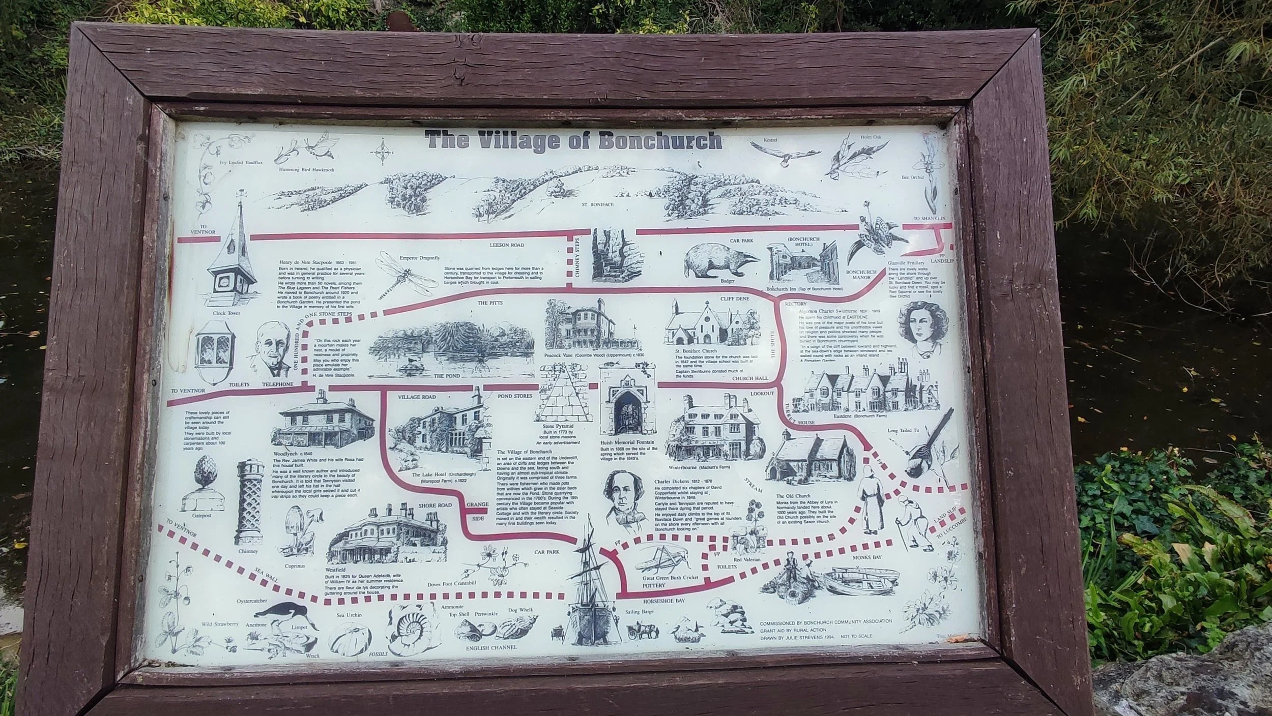 Map of The Village of Bonchurch showing landmarks, streets, and illustrations of local wildlife and historical figures, set in a wooden frame outdoors.