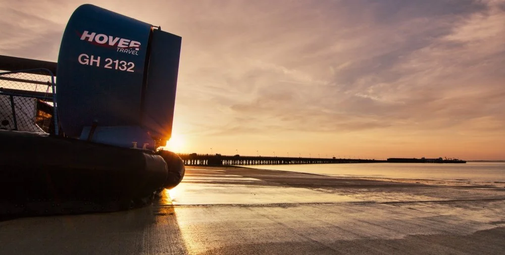 A hovercraft on a sandy beach at sunset with a pier in the distance.