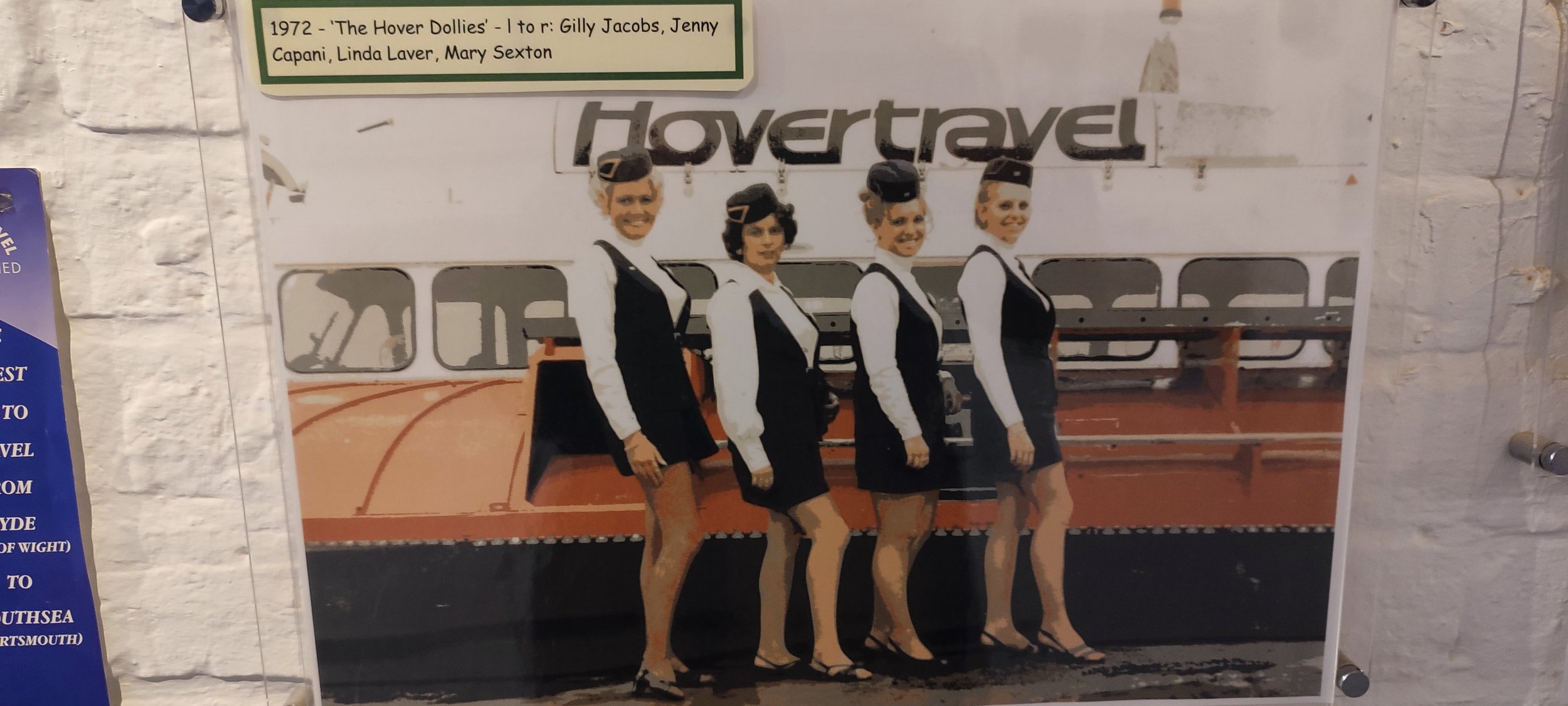 Vintage photo of four flight attendants in uniform standing in front of a hovercraft with the word 'hovertravel' on it, dated 1972.